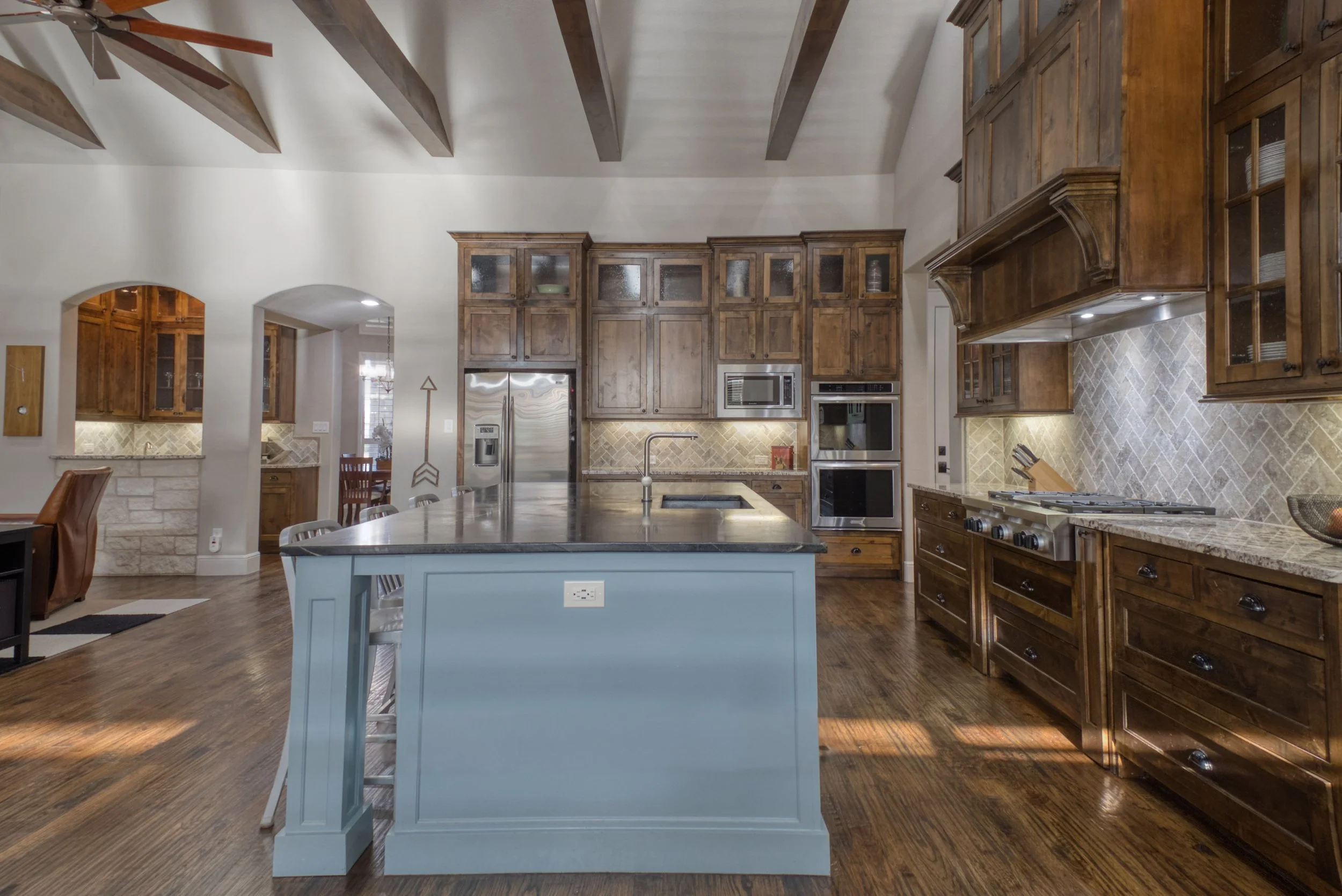 Modern kitchen with wooden cabinets, a large island with a dark countertop, stainless steel appliances, and a herringbone backsplash.