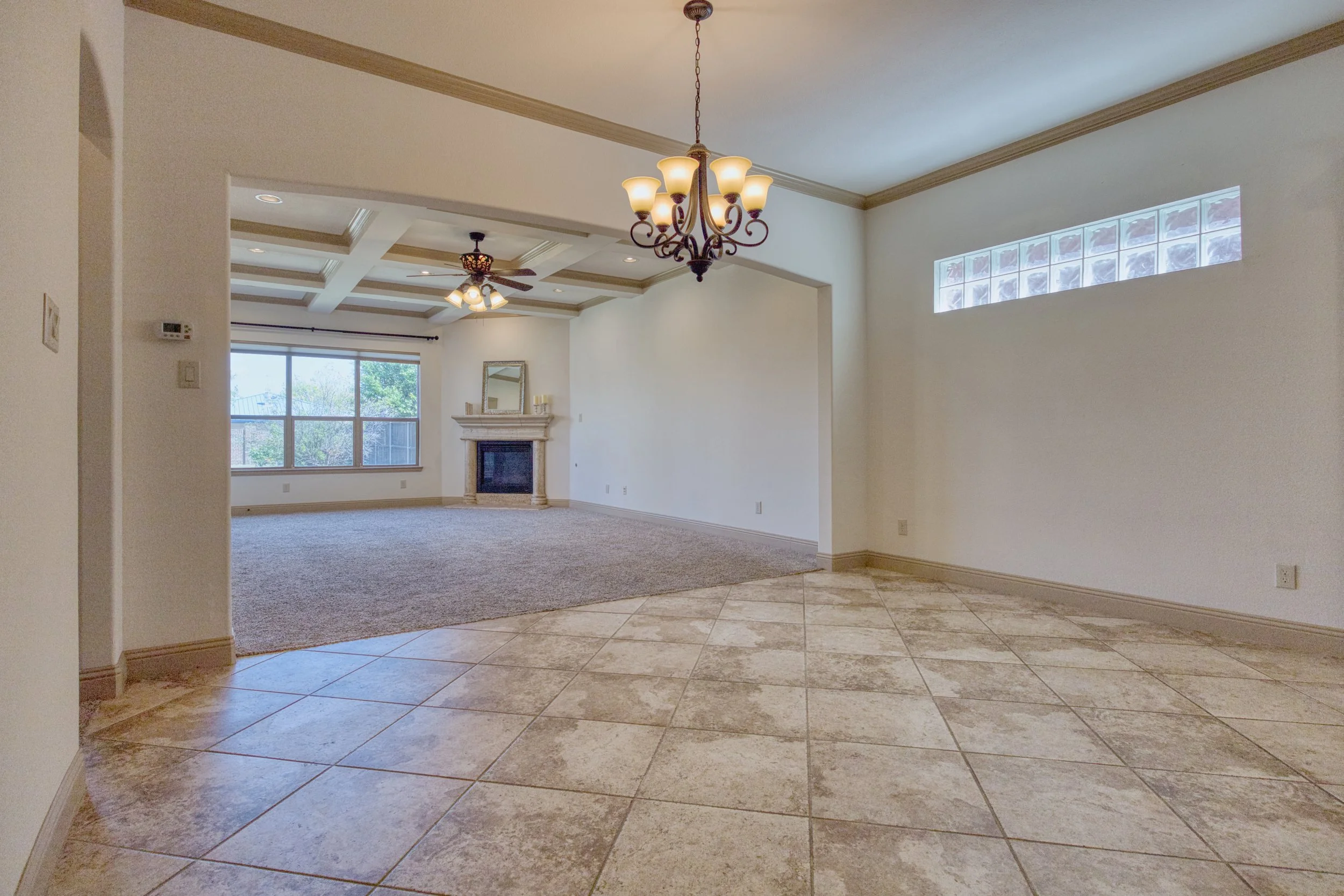 Open living room with tiled floor, carpeted area, chandelier, vaulted ceiling with ceiling fans, large window, and fireplace.