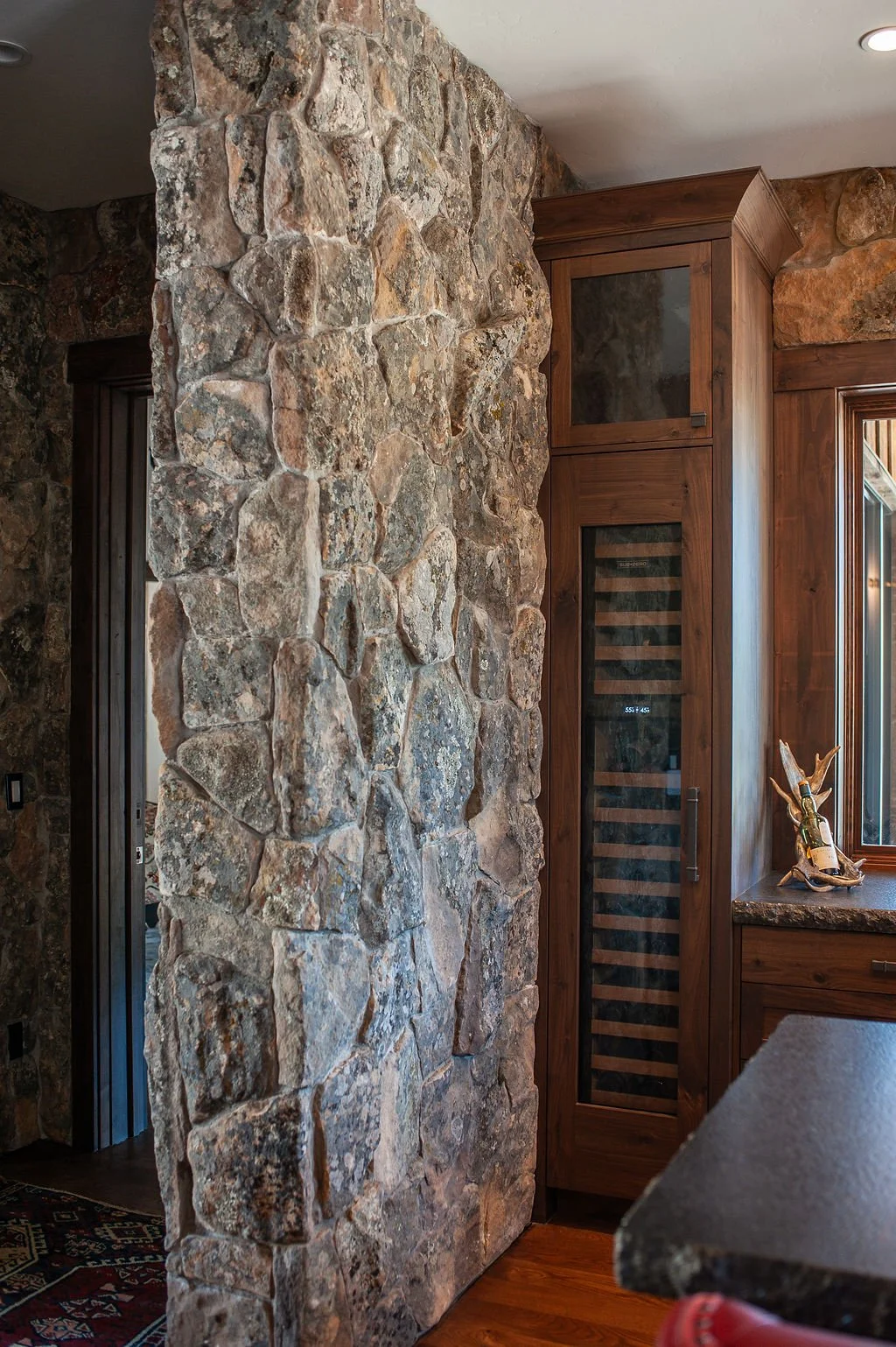 A stone wall and a wooden wine cabinet with glass door in a rustic kitchen interior.
