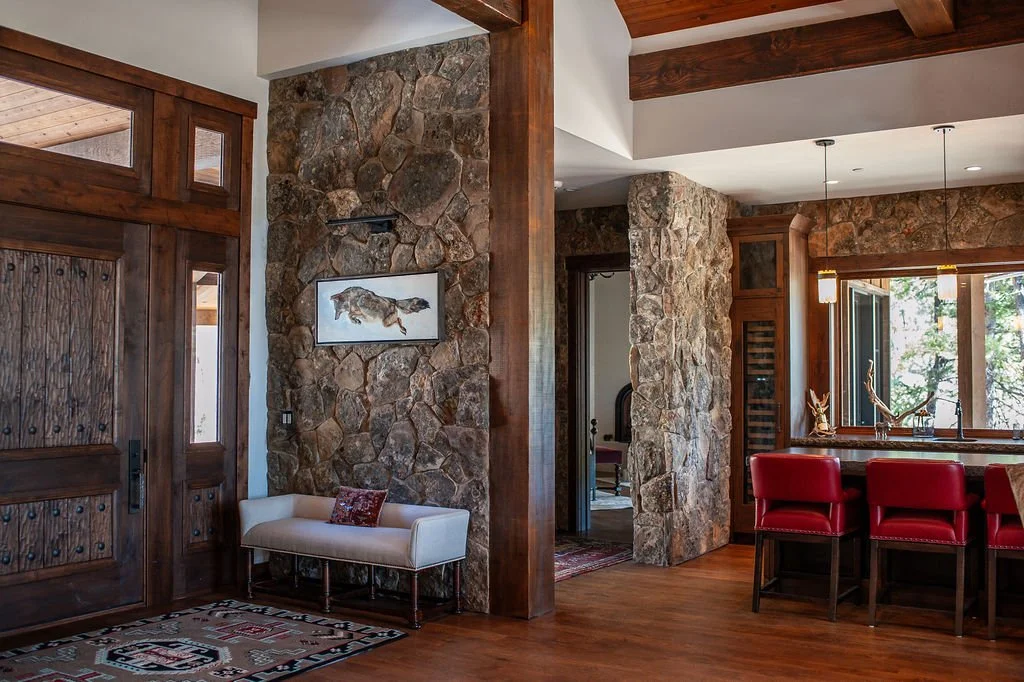 Interior view of a rustic living space with stone walls, wooden accents, red bar stools, and a painting of a fish on the wall.