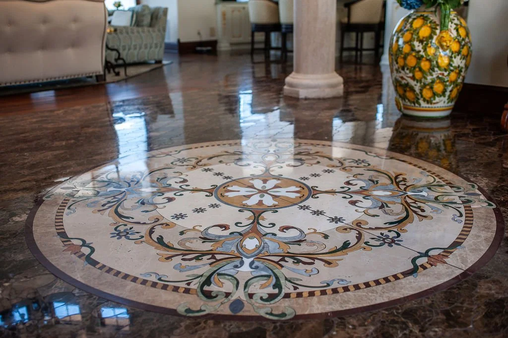 Decorative circular marble floor medallion with intricate floral and scroll patterns in beige, blue, and gold, in a spacious living area.