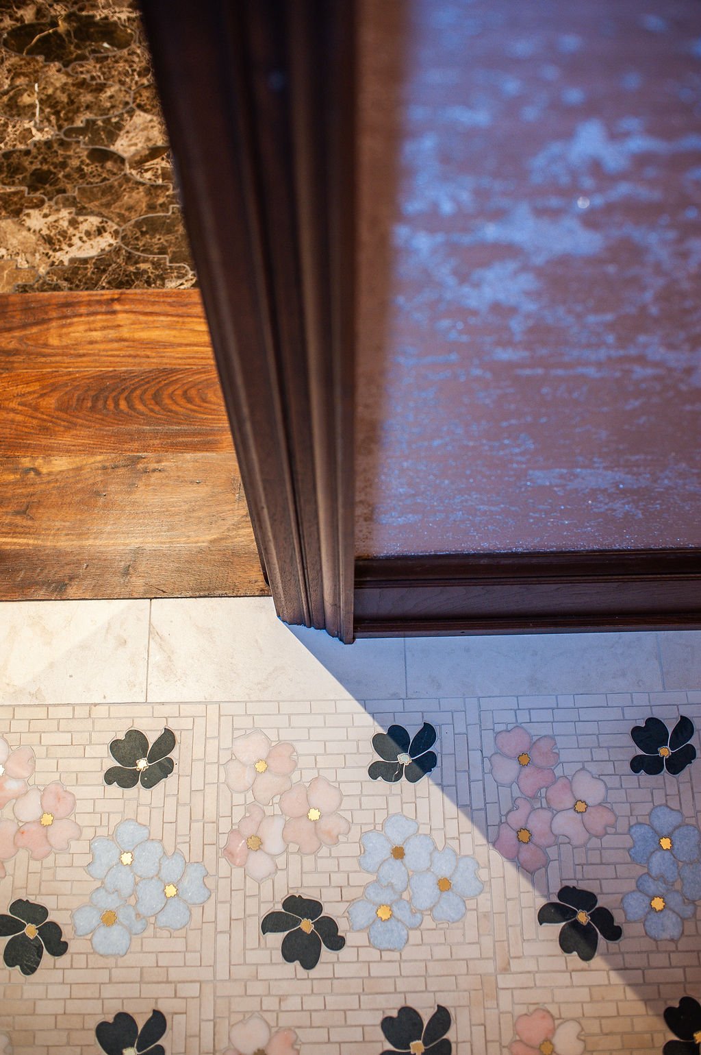 Part of a wooden cabinet or furniture piece, a marble countertop, and patterned floor tiles featuring pink, white, and black flower designs with yellow centers.