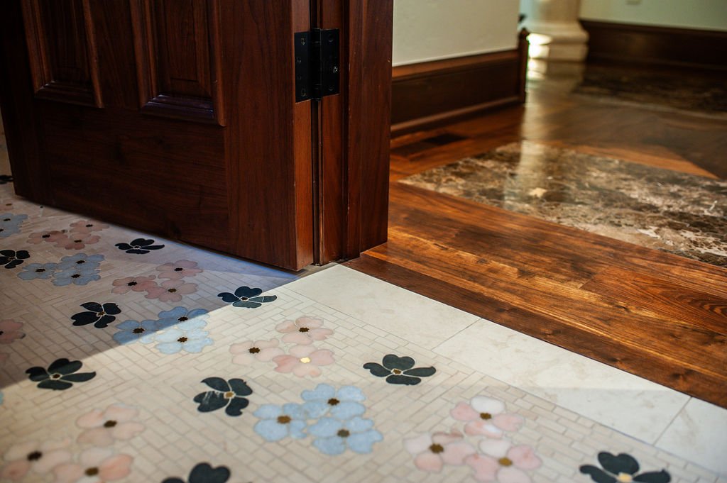 Close-up of the corner where a wooden door frame meets a tiled floor with floral pattern transitions to hardwood flooring.