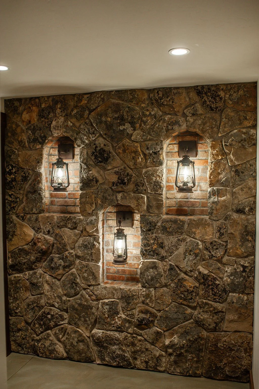 Interior stone wall with three vintage lanterns mounted in niches with a brick background, illuminated and contrasting with the dark stone.