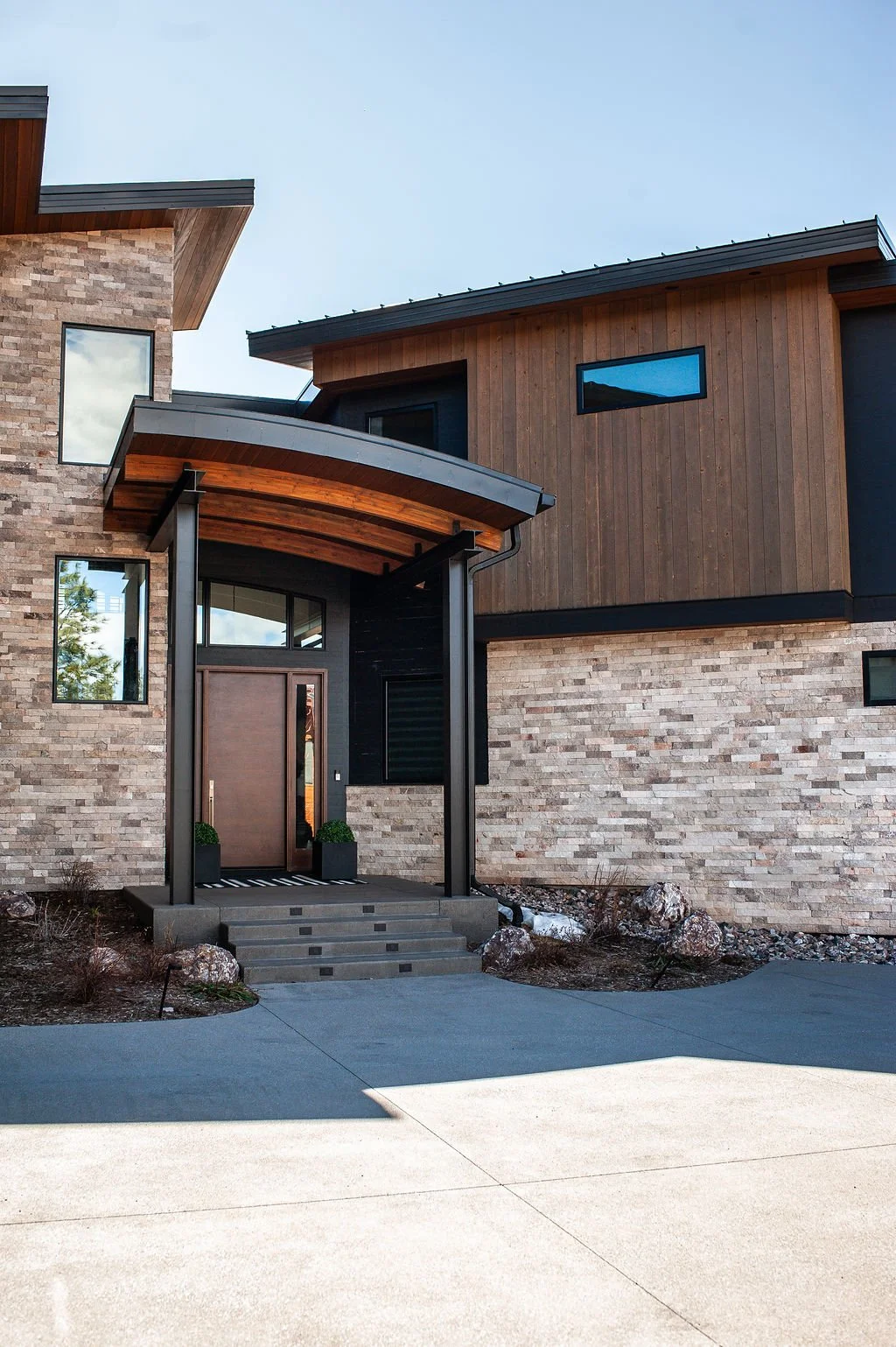 Exterior of a modern house with brick and wooden siding, a covered porch with steps, and large windows.