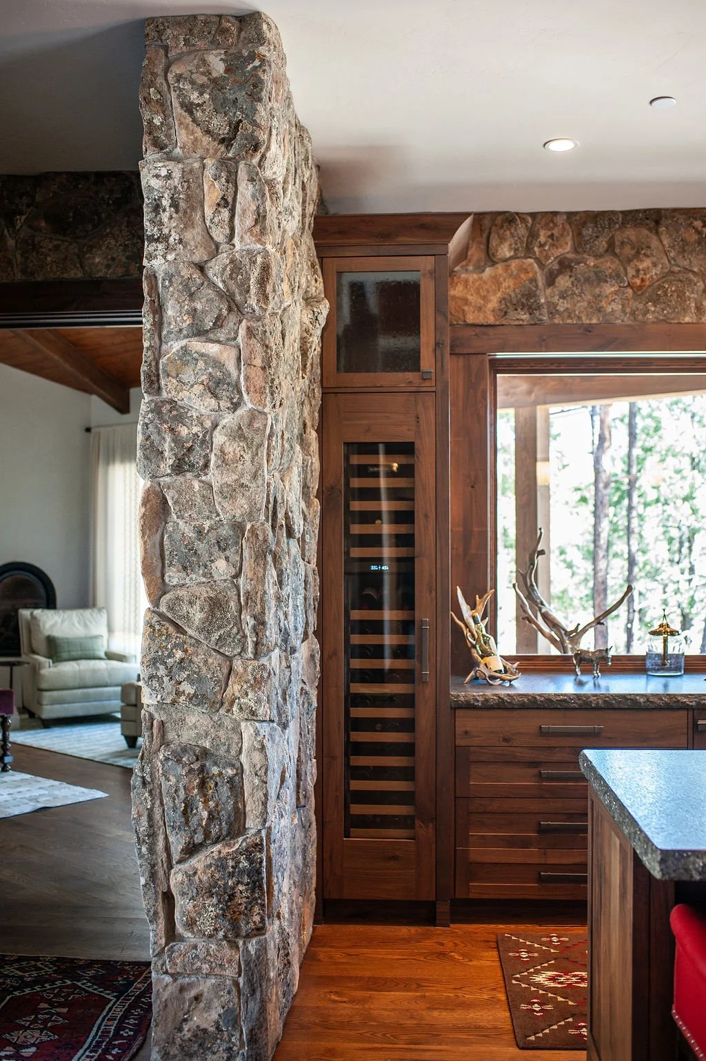 Interior view of a house showing a stone wall, wooden cabinetry, and a window with a forest scene outside.