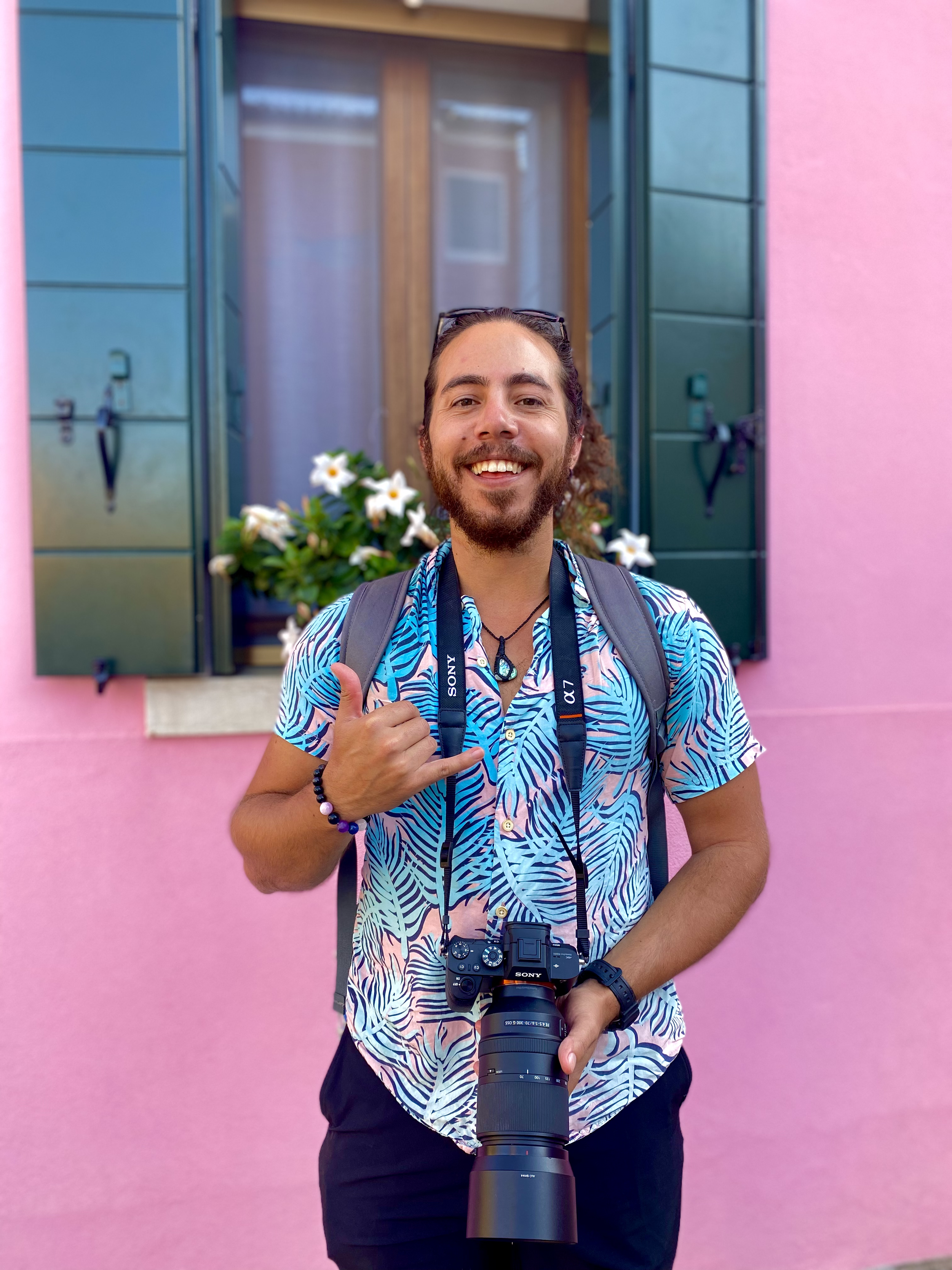 A photo of myself (Jonathan Fisk) standing and smiling, with one hand holding up a shaka and the other supporting the camera draped around my neck