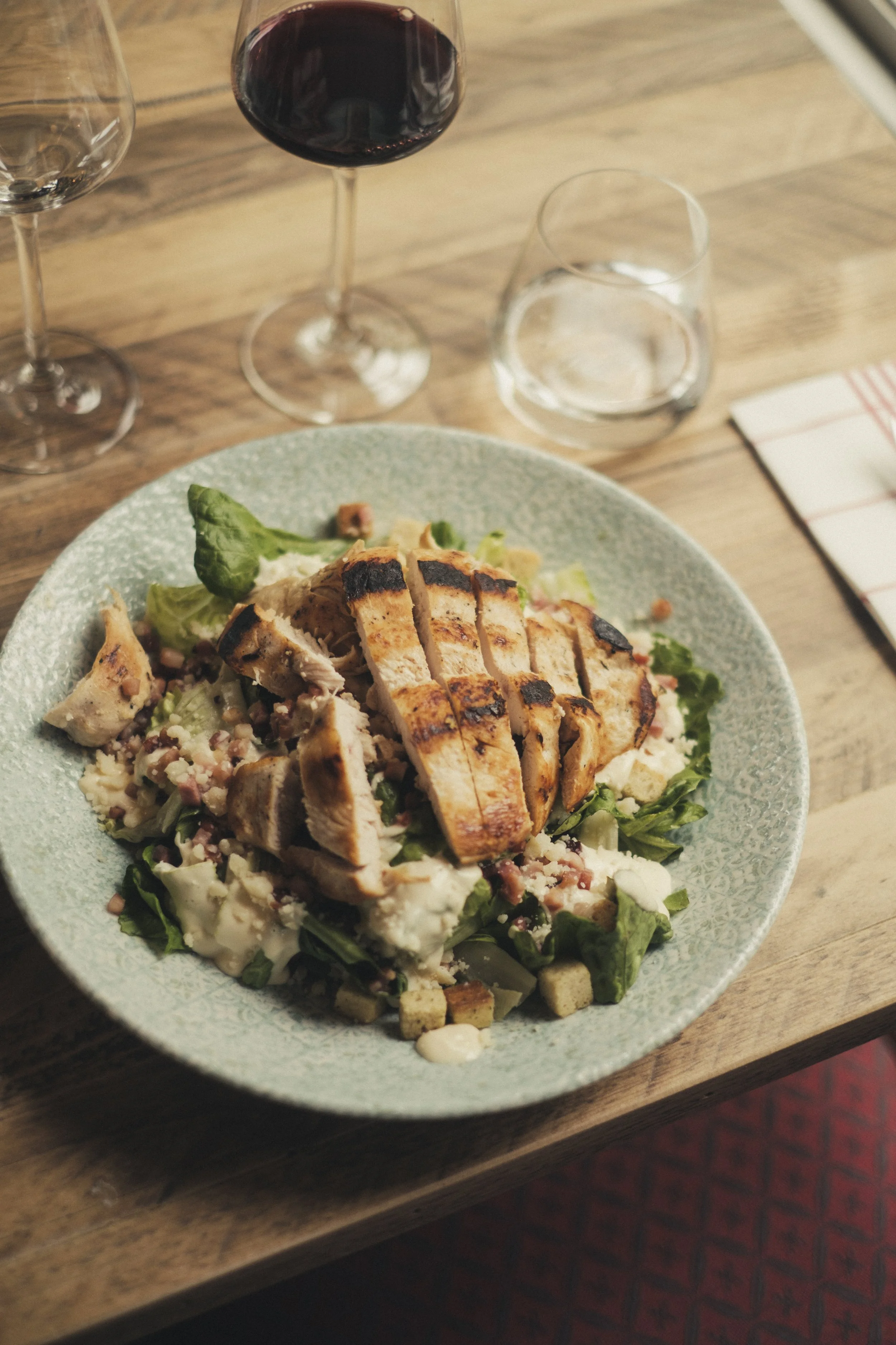 Cæsarsalat med grillet kyllingbryst, salat, ost og krutonger på bordet med et glass rødvin. - Bygdøy Vertshus