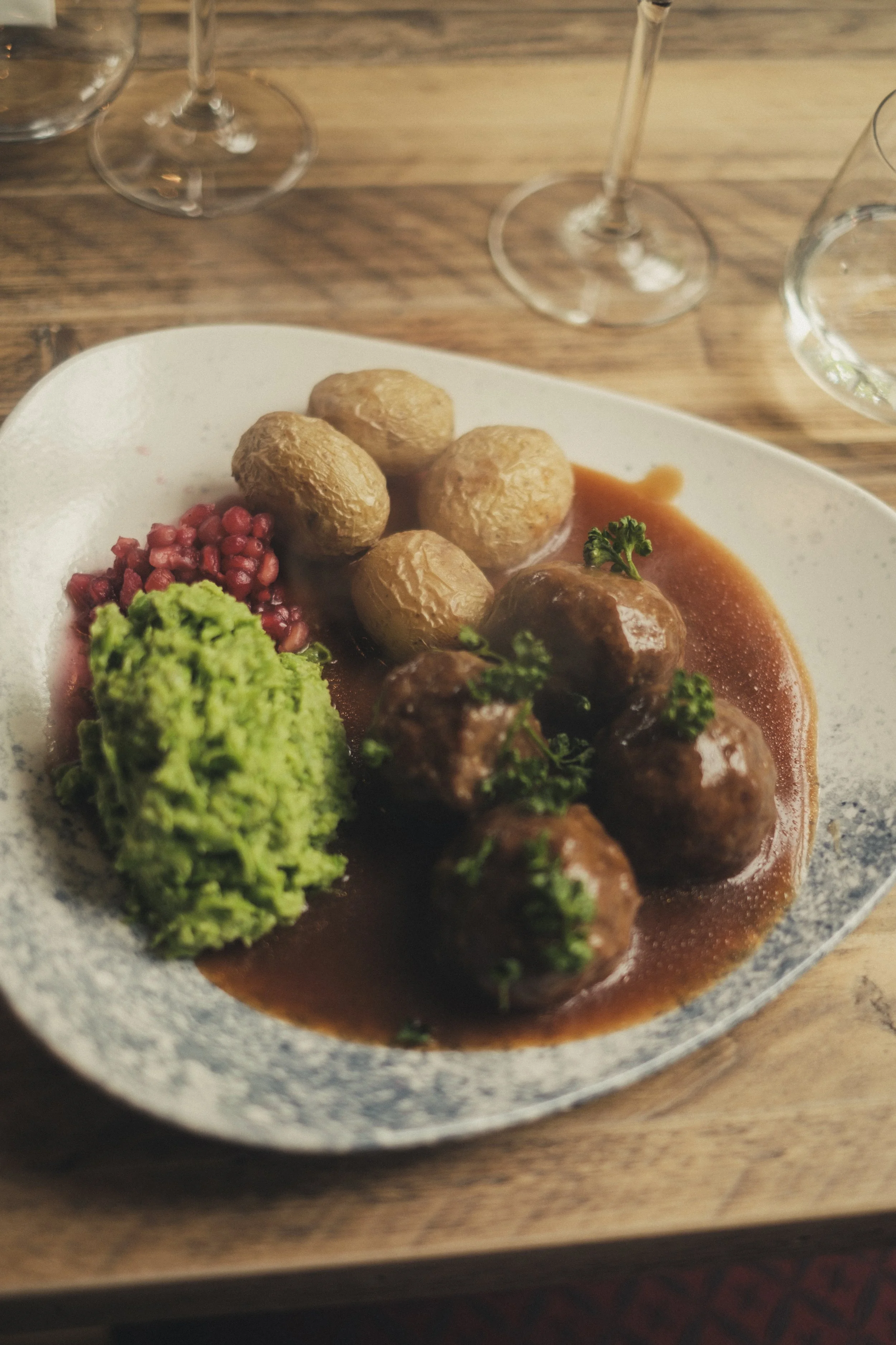 Kjøttkaker i brunsaus med grønn ertepuré og poteter på tallerken med rødvin på bordet - Bygdøy Vertshus