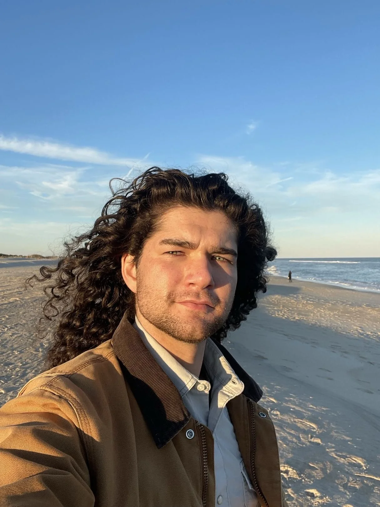 Evan Smith taking a selfie on the beach in Assateague National Seashore. His face is lit with an orange-ish tone, due to facing into the sunset.