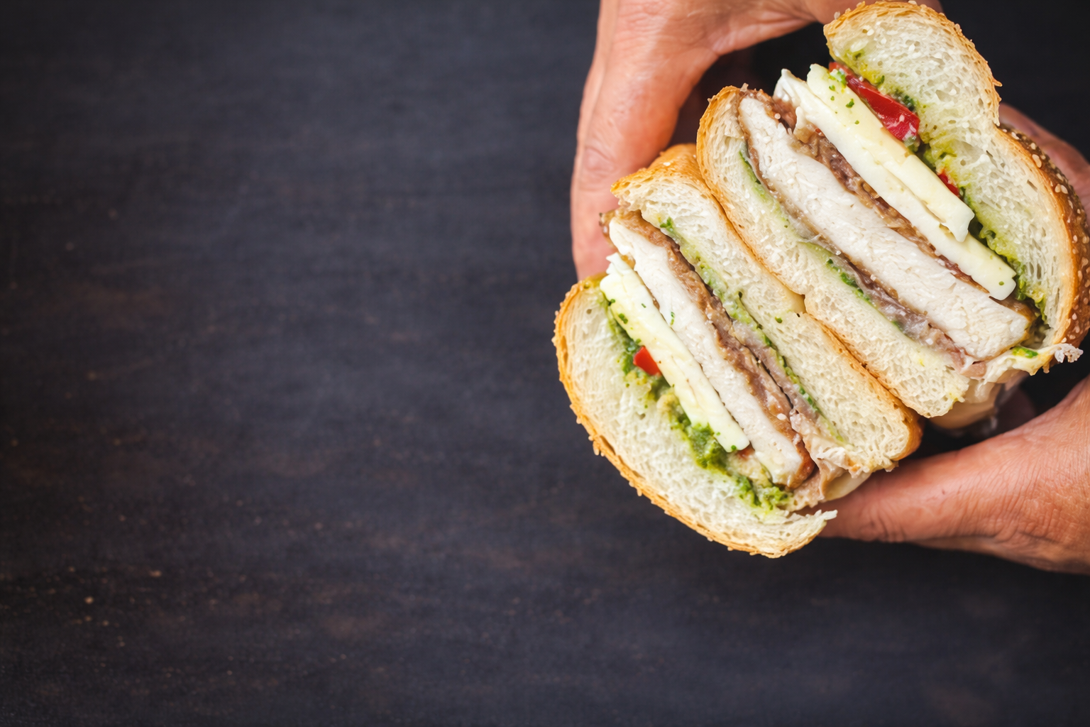 Hands holding a crispy and juicy Cutlets, Fresh Mozzeralla, Roast Peppers, Prosciutto & arugula puree.