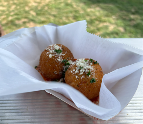 Two fried Italian arancini balls sprinkled with grated cheese and herbs in a paper liner