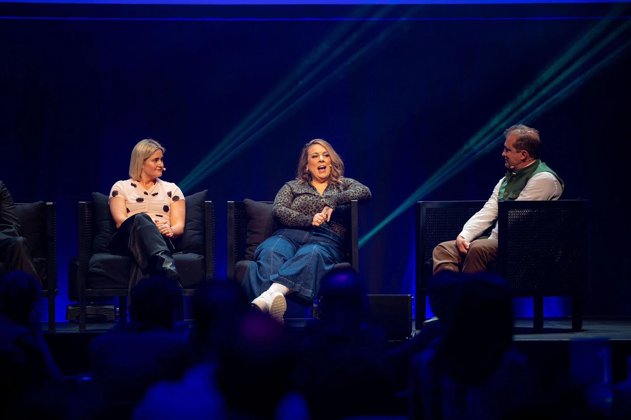 Revved panel sitting on stage in conversation, with a dark background and blue lighting.