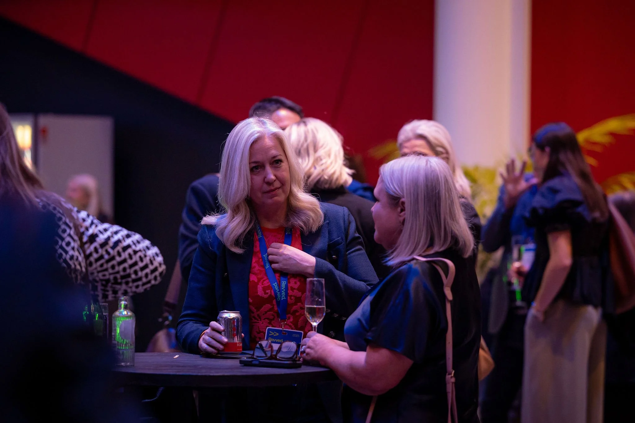 A group of women socializing at a reception or conference, with drinks and decorations visible.