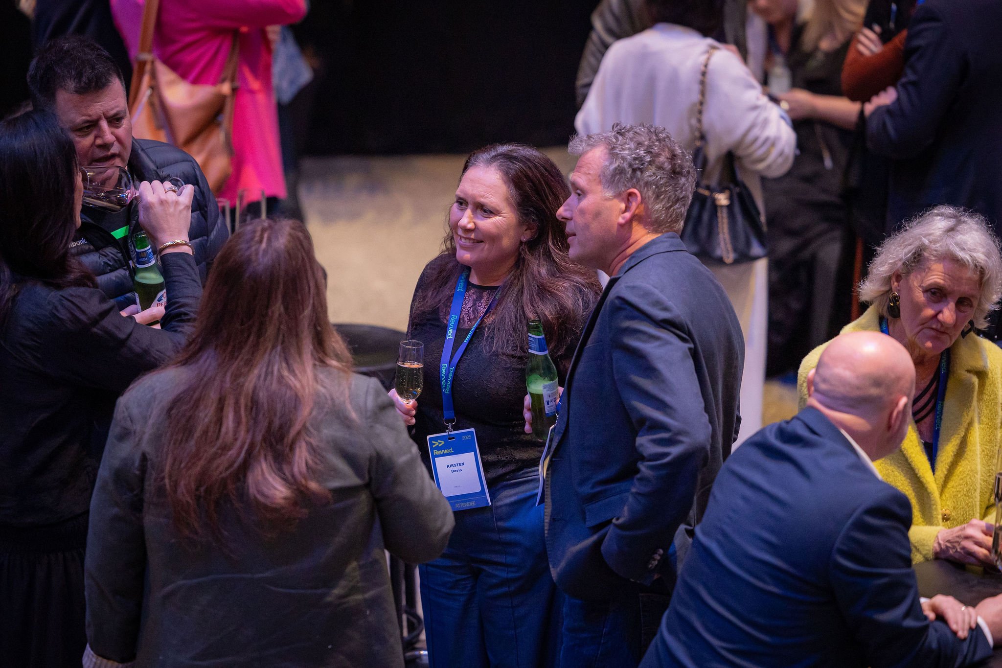 People socializing at an indoor event, some holding drinks and wearing name badges.
