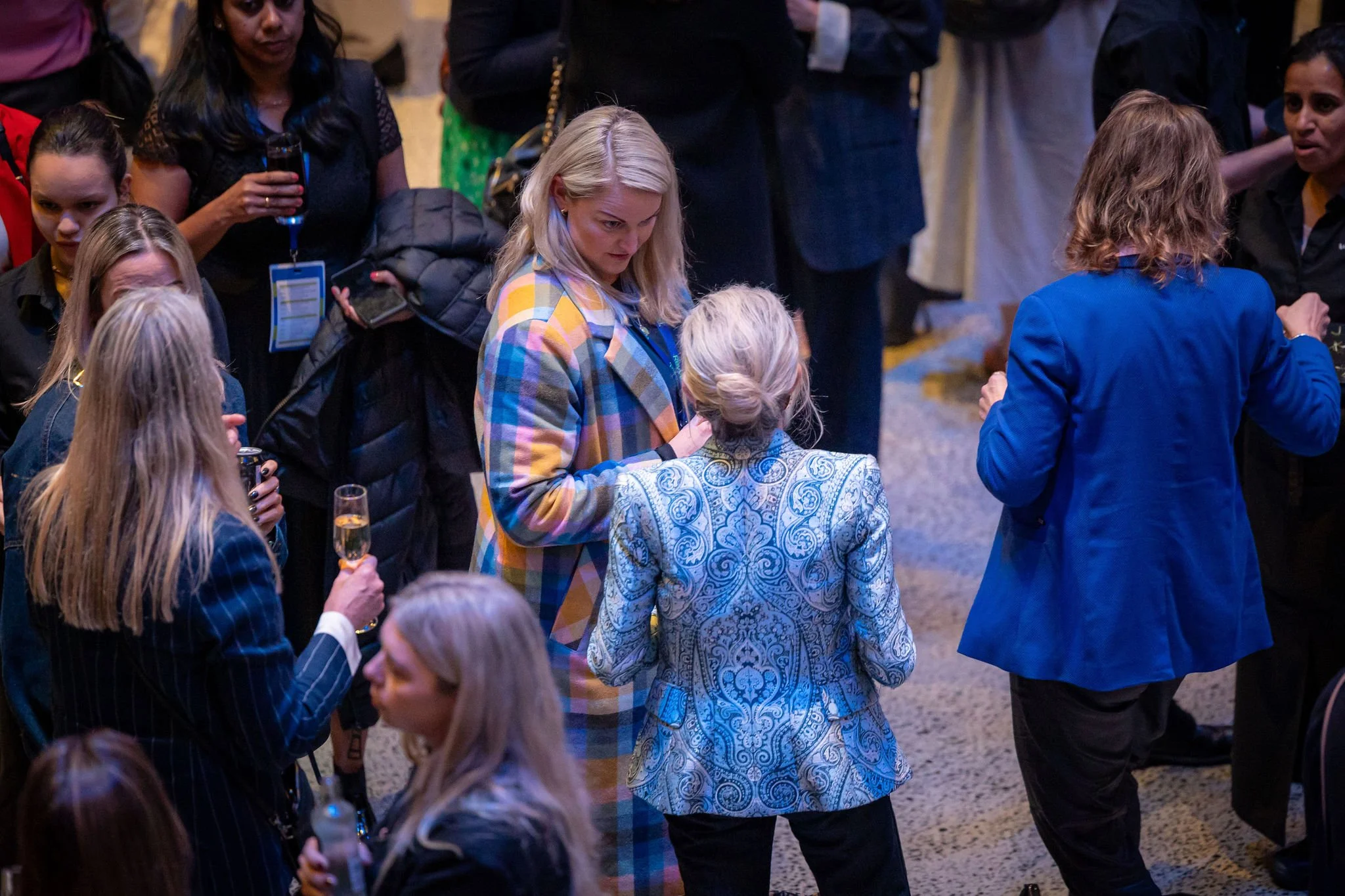Group of people gathered at an indoor event, some holding drinks, engaged in conversations.