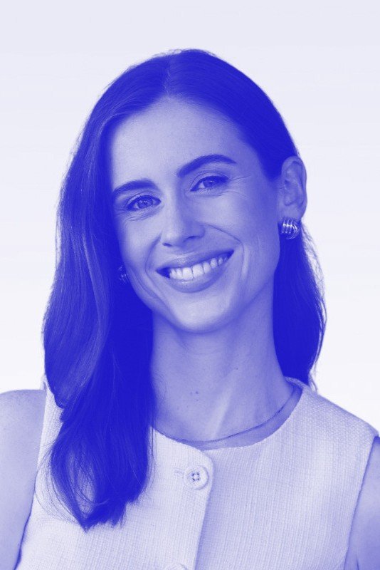 A smiling woman with dark hair wearing a sleeveless top and earrings, against a light background.