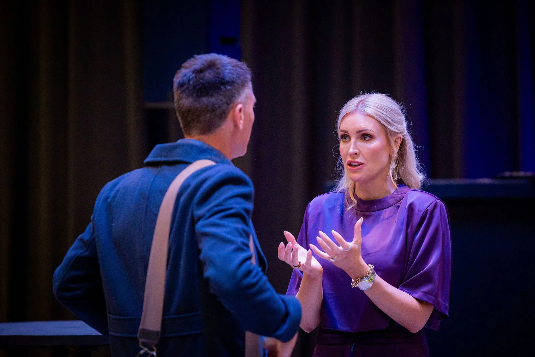 A man and woman engaged in conversation, with the woman gesturing with her hands.