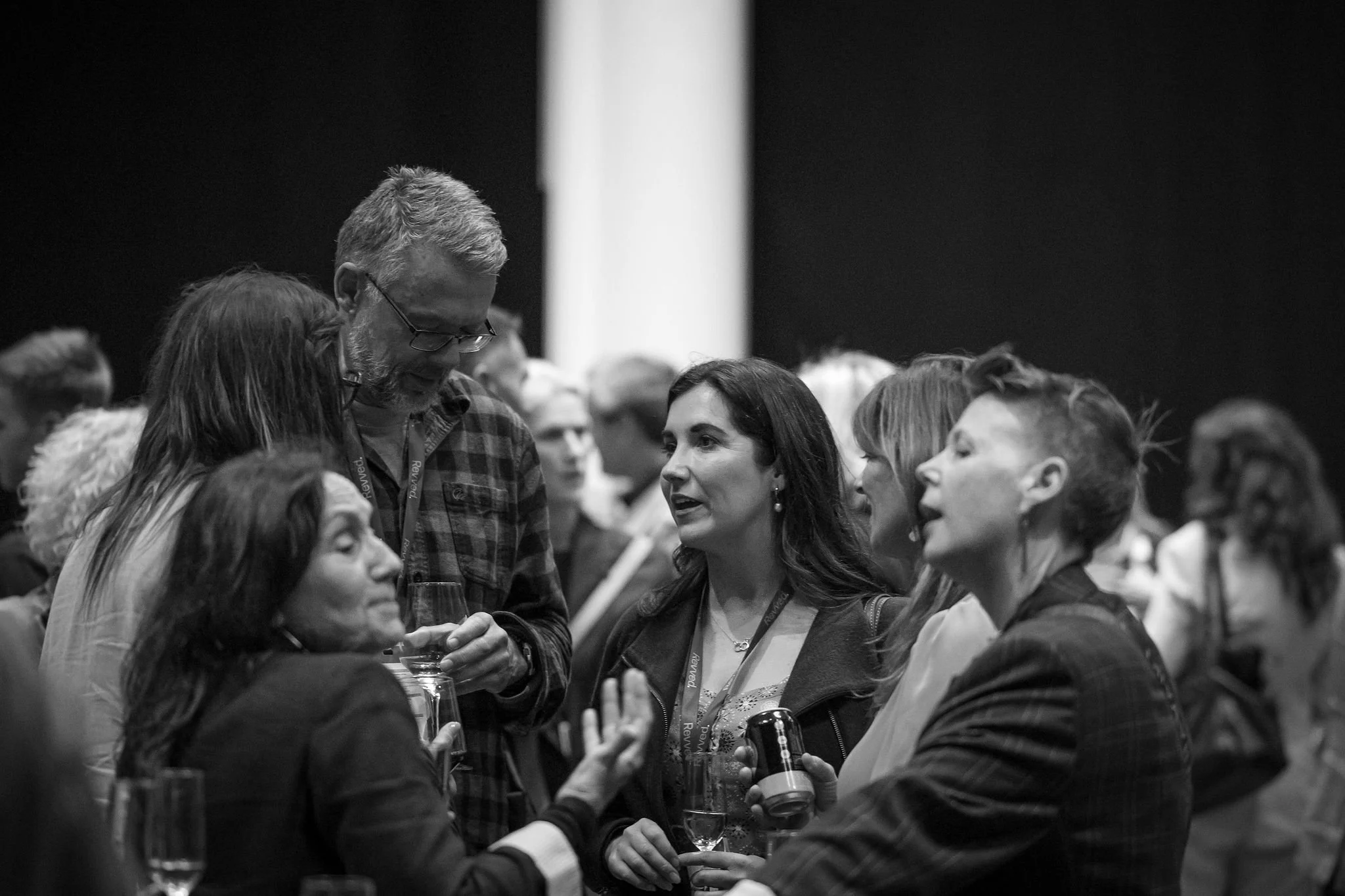 Group of people engaged in conversation at a social event, some holding glasses of wine or drinks.
