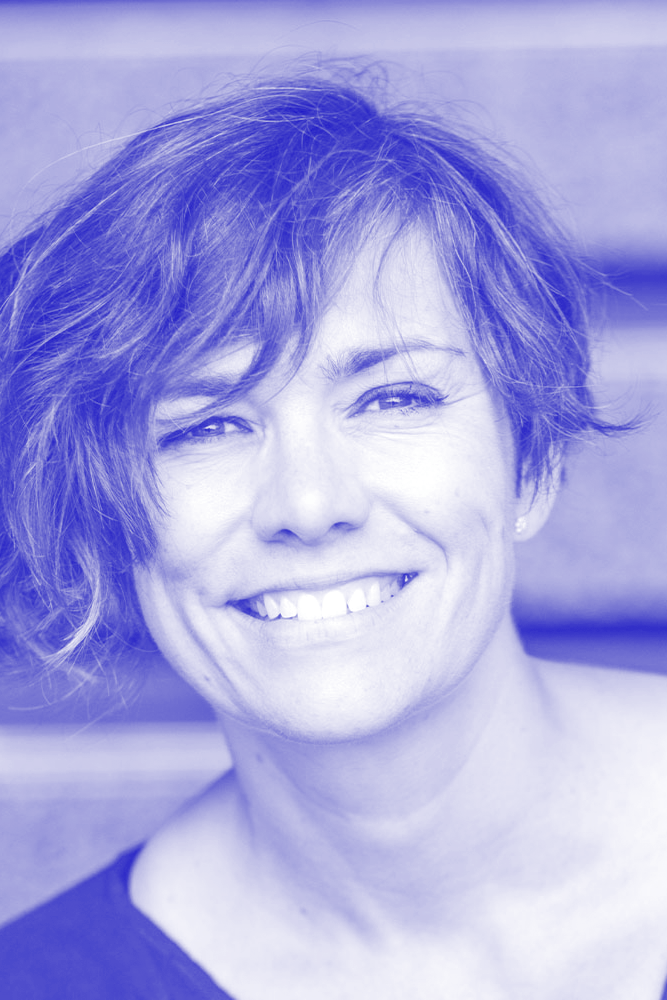 A woman with short, wavy hair smiling at the camera with a blurred background.