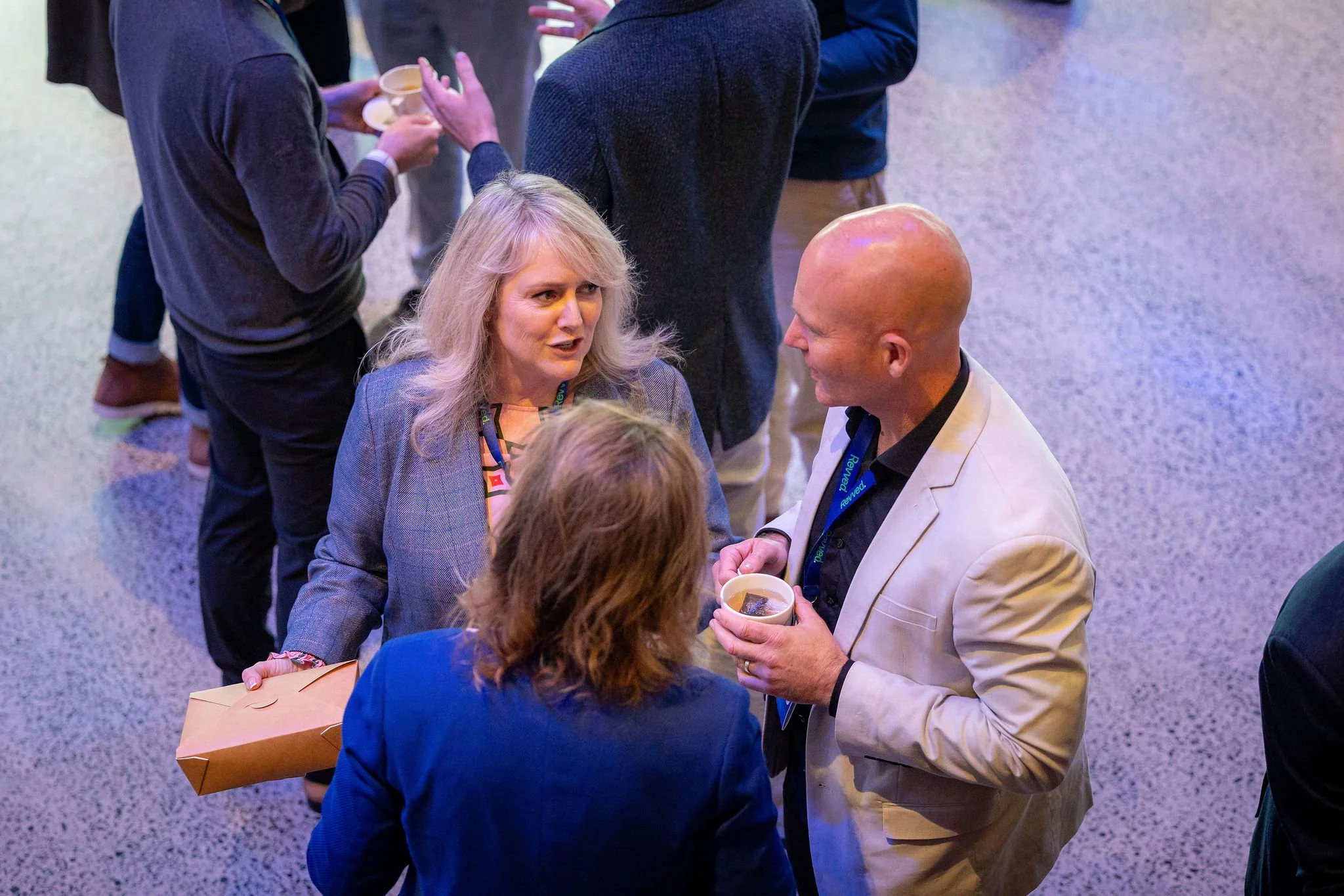Group of people engaging in conversation at a social event, with one person holding a cup and engaging with others in discussion.