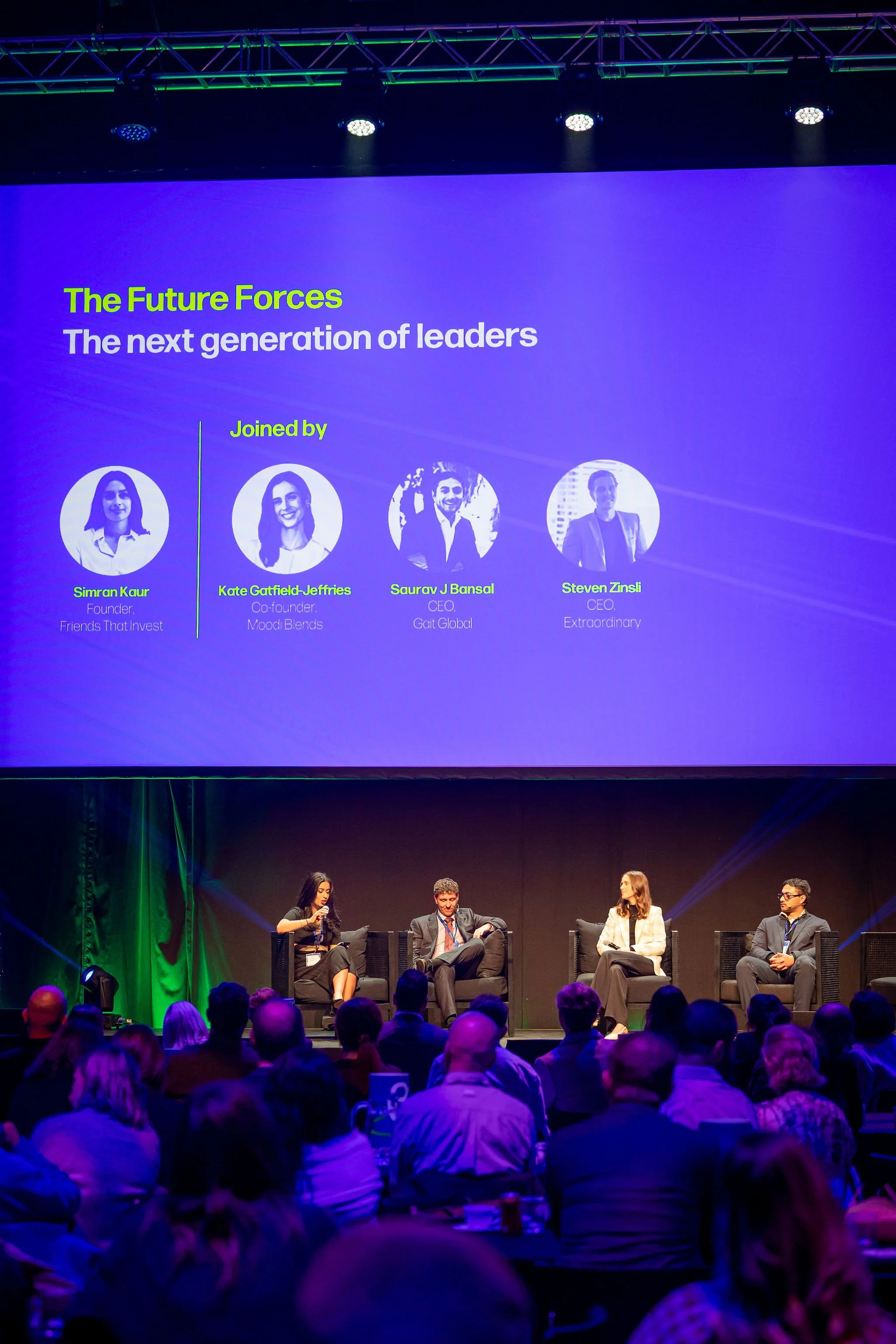A panel discussion at a conference with four panelists seated on stage. A large screen behind them displays the event title, 'The Future Forces: The next generation of leaders,' along with photos and names of the speakers: Simran Kaur, Kate Gaffield-