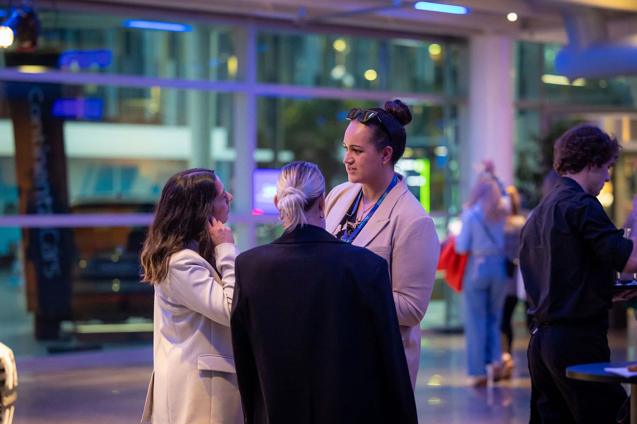 Group of four women engaged in conversation at a social event in a modern indoor venue with colorful lighting