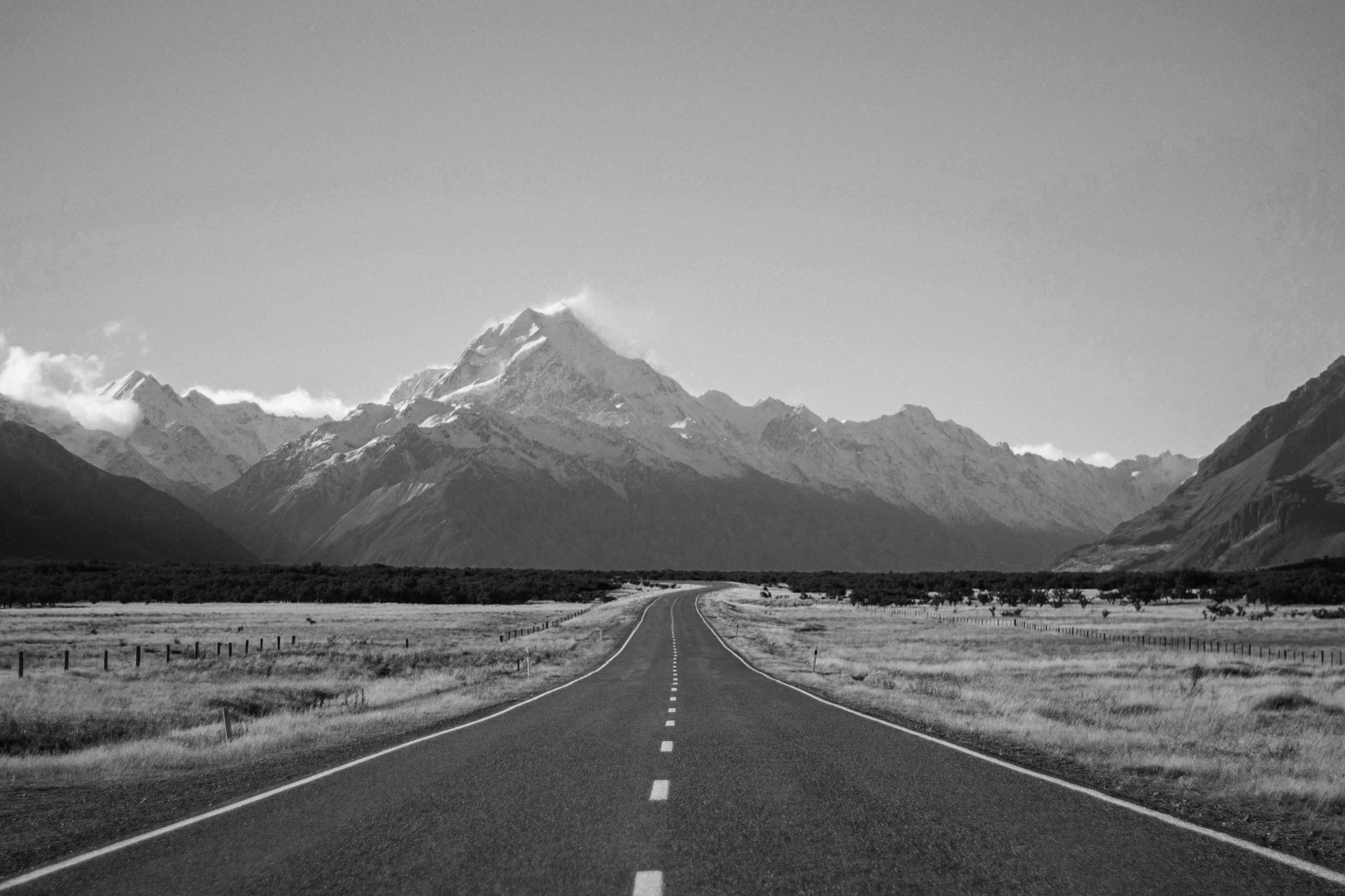 An open road leading toward New Zealand's snow-capped mountains.