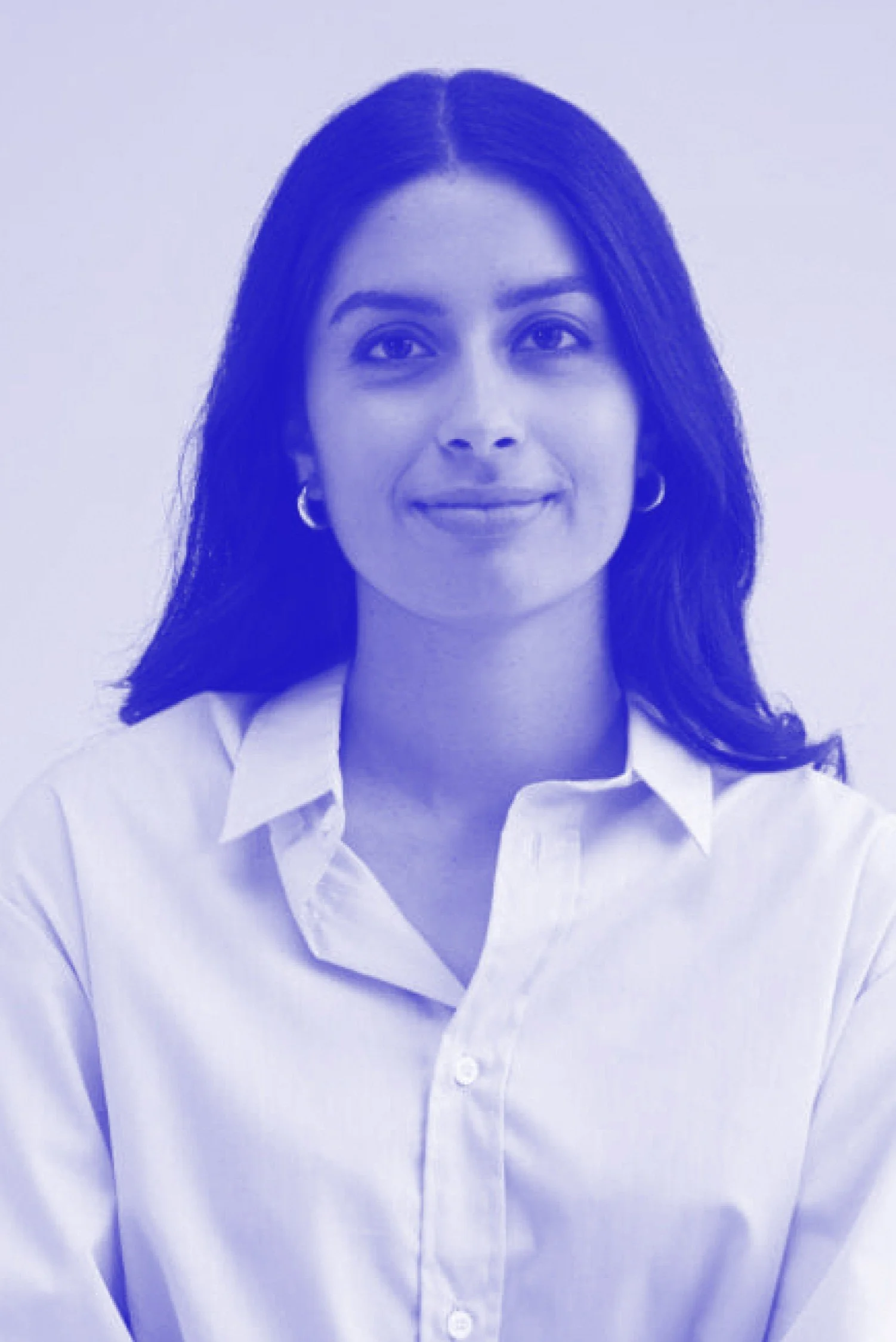A woman with dark hair, wearing a white button-down shirt, smiling softly against a plain background.