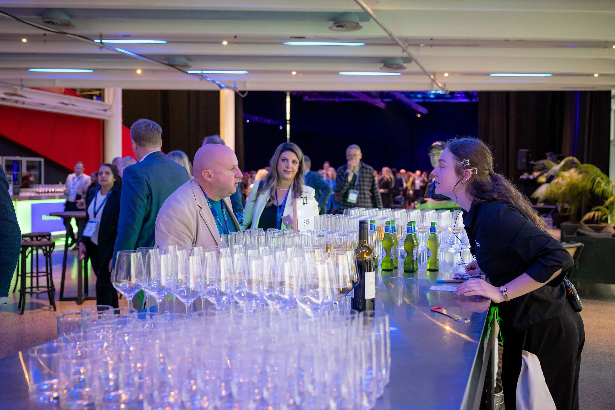 Event with a bar serving drinks,ção background with people socializing and staff preparing beverages.