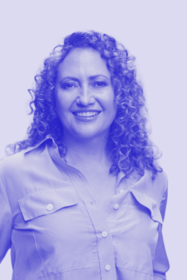 A woman with curly hair smiling, wearing a button-up shirt against a light background.