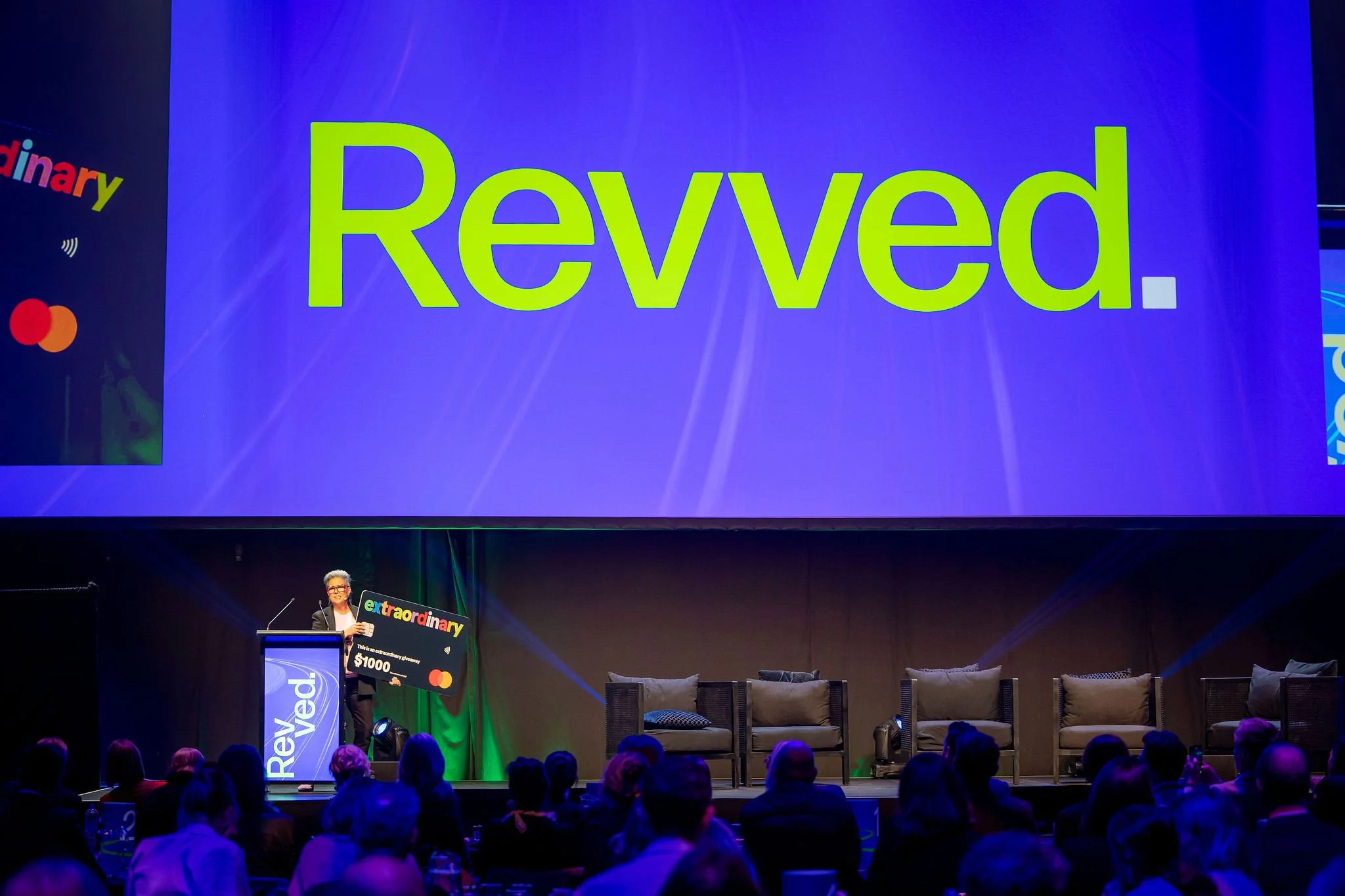 A large presentation screen displaying the word 'Revved' in bright green letters on a blue background.