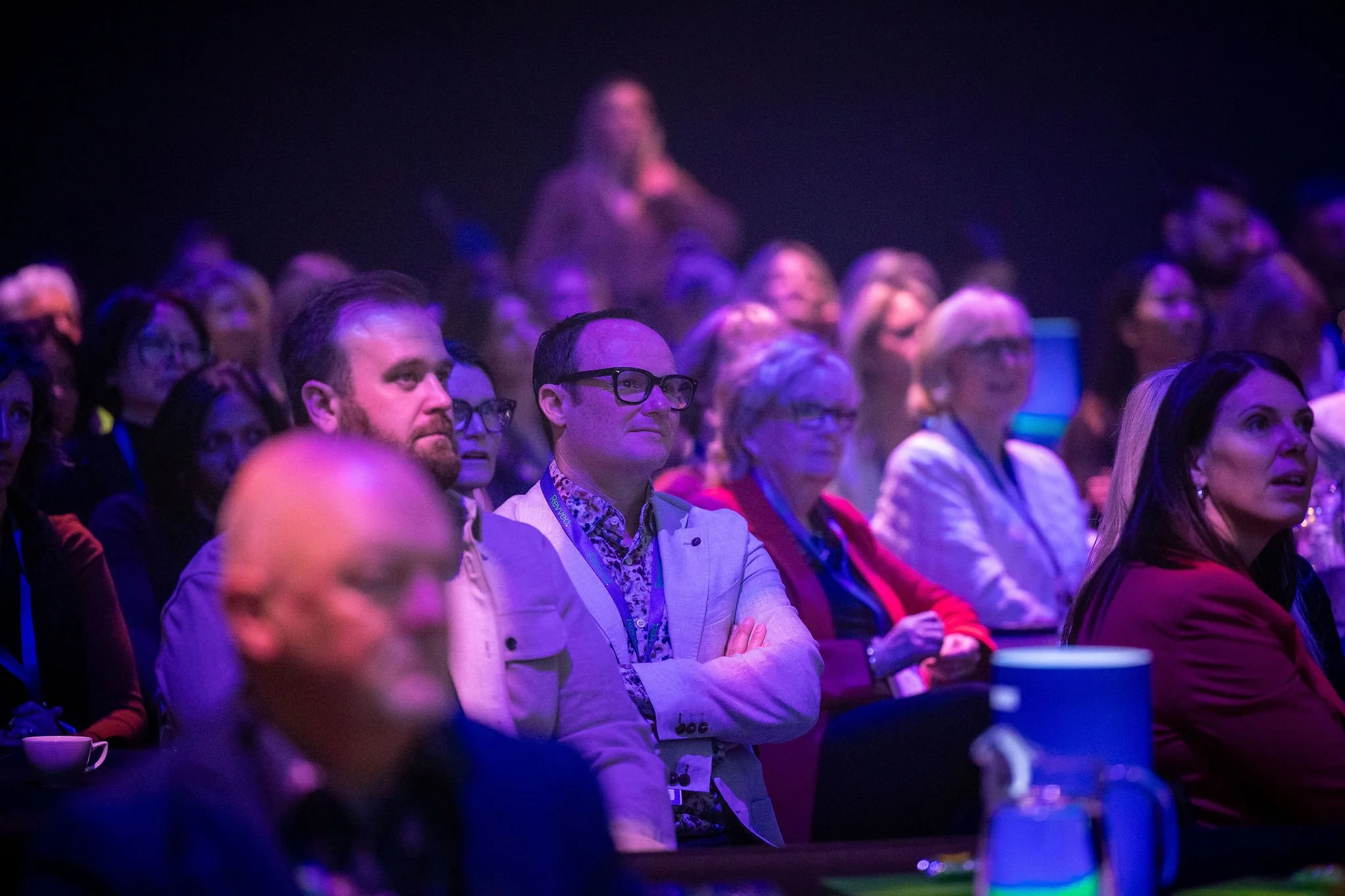 Audience attentively listening at Revved with purple and blue lighting.