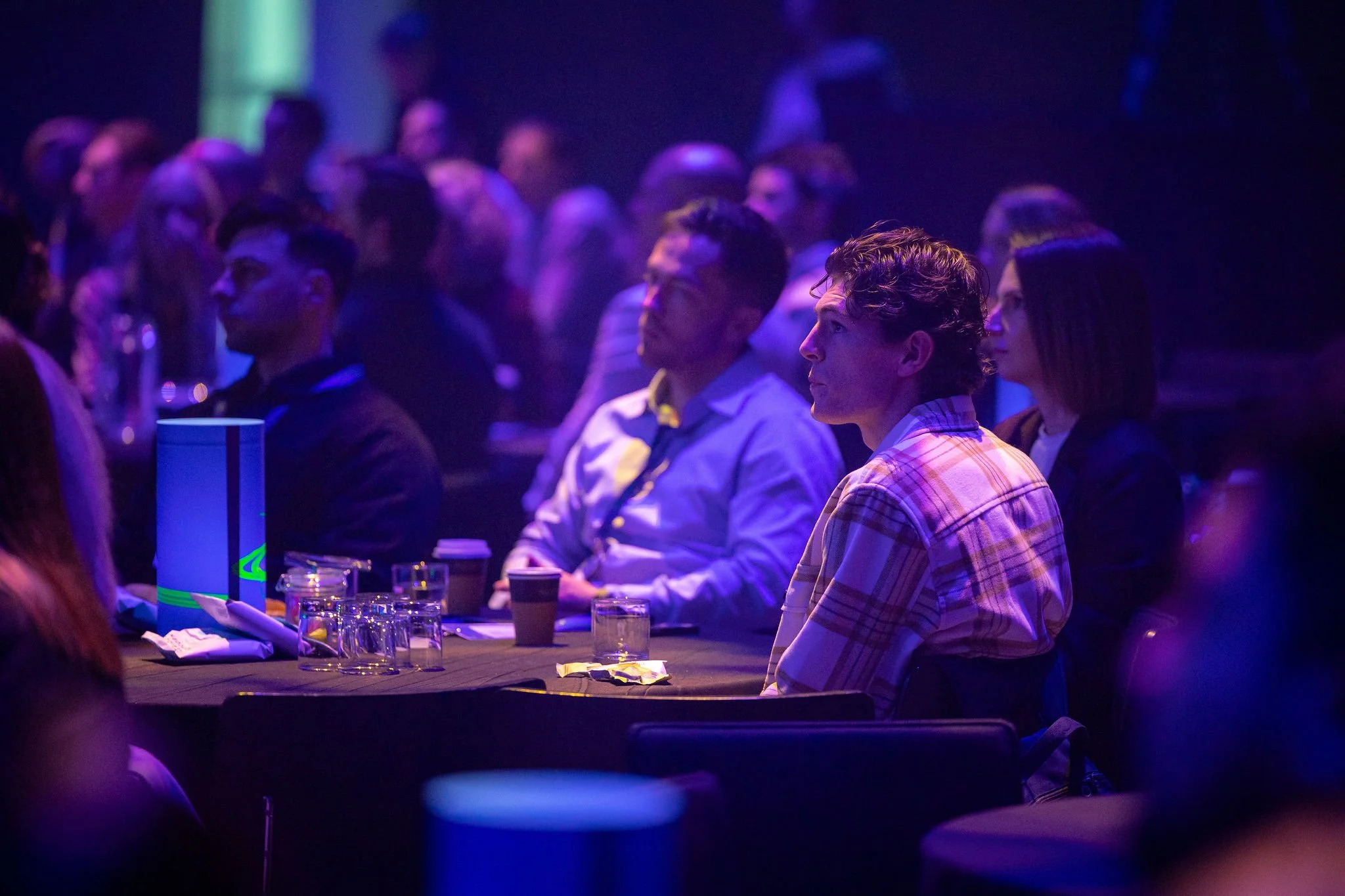 Revved audience members seated at tables under purple lighting