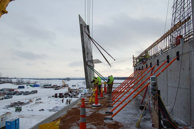 Construction workers install a large solar panel on a building roof during winter, with snow-covered ground and a cloudy sky in the background.