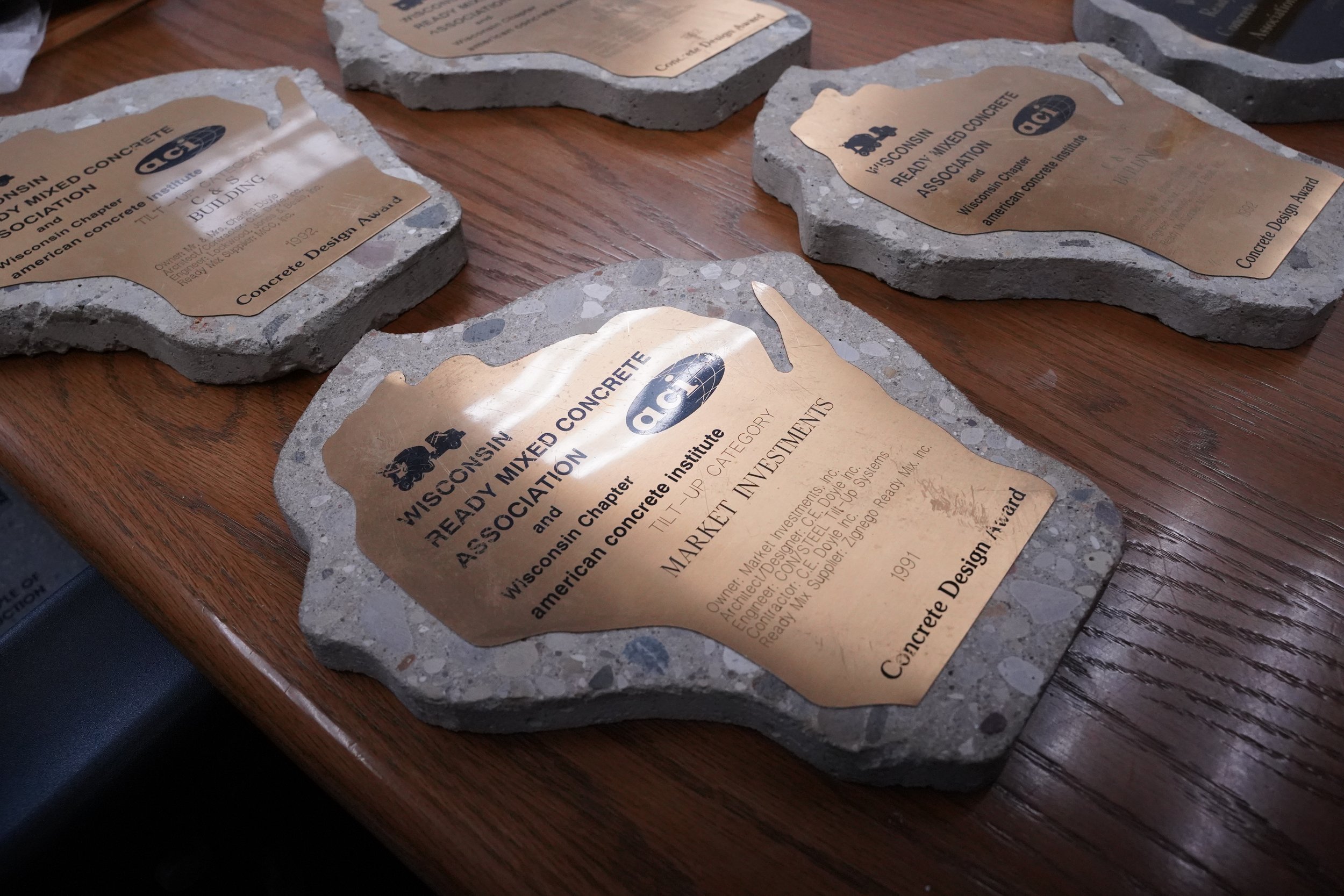 Metal plaques on rough stone bases, engraved with text about the Wisconsin Ready Mixed Concrete Association, placed on a wooden surface.