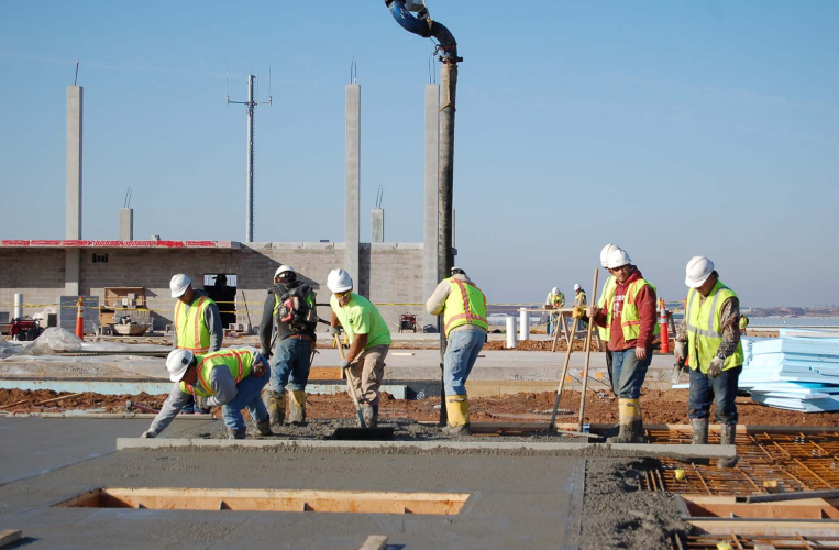 Construction workers in safety vests and helmets pouring concrete on a building site.