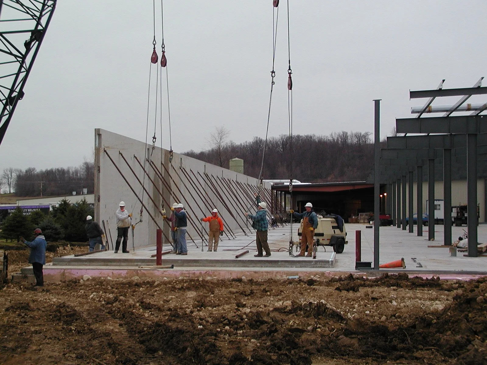 Construction workers installing a concrete wall on a building site under gray skies.