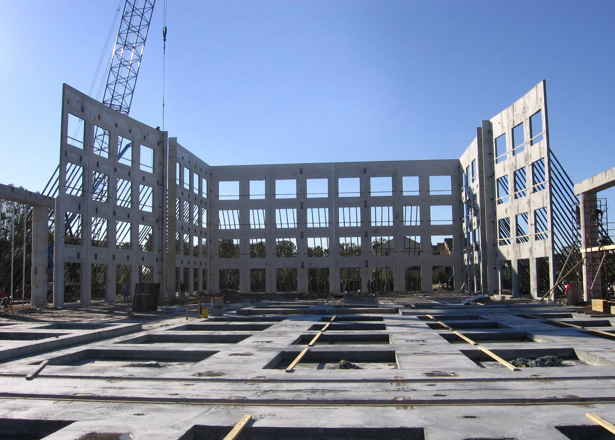 Construction site with wooden framework for a building, a crane in the background, and blue sky.