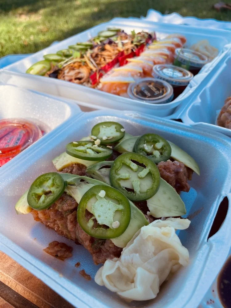 Close-up of sushi tray with jalapeño on top and a side of wasabi, with another sushi tray and soy sauce in the background