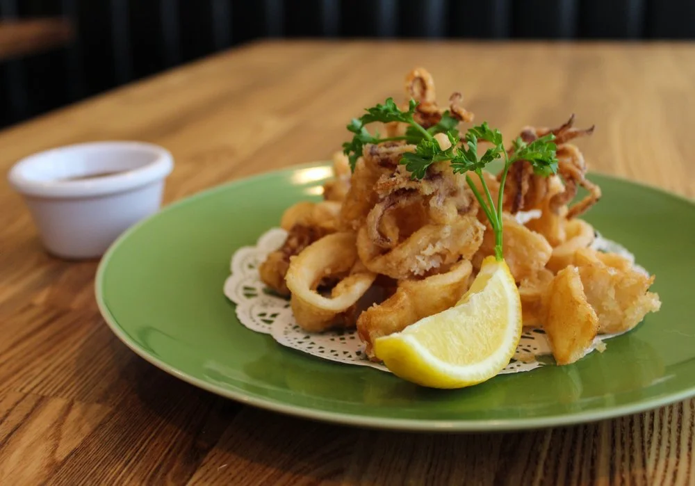 Fried calamari on a green plate garnished with lemon wedge and parsley, with a small bowl of dipping sauce on the side.