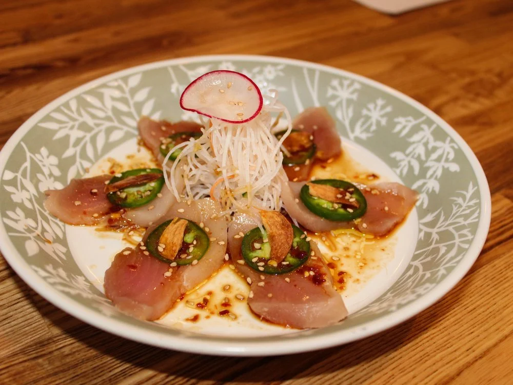 Vietnamese rice paper salad with sliced chicken, jalapeño slices, shredded vegetables, chopped garlic, and sesame seeds on a patterned plate.