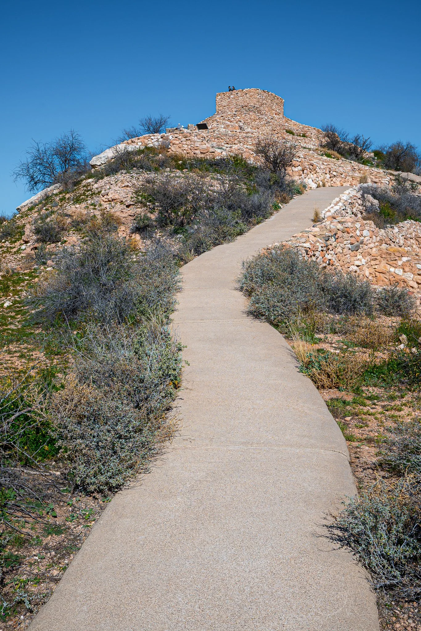 A winding pathway leading to a rocky hilltop with an old stone structure, under a clear blue sky.