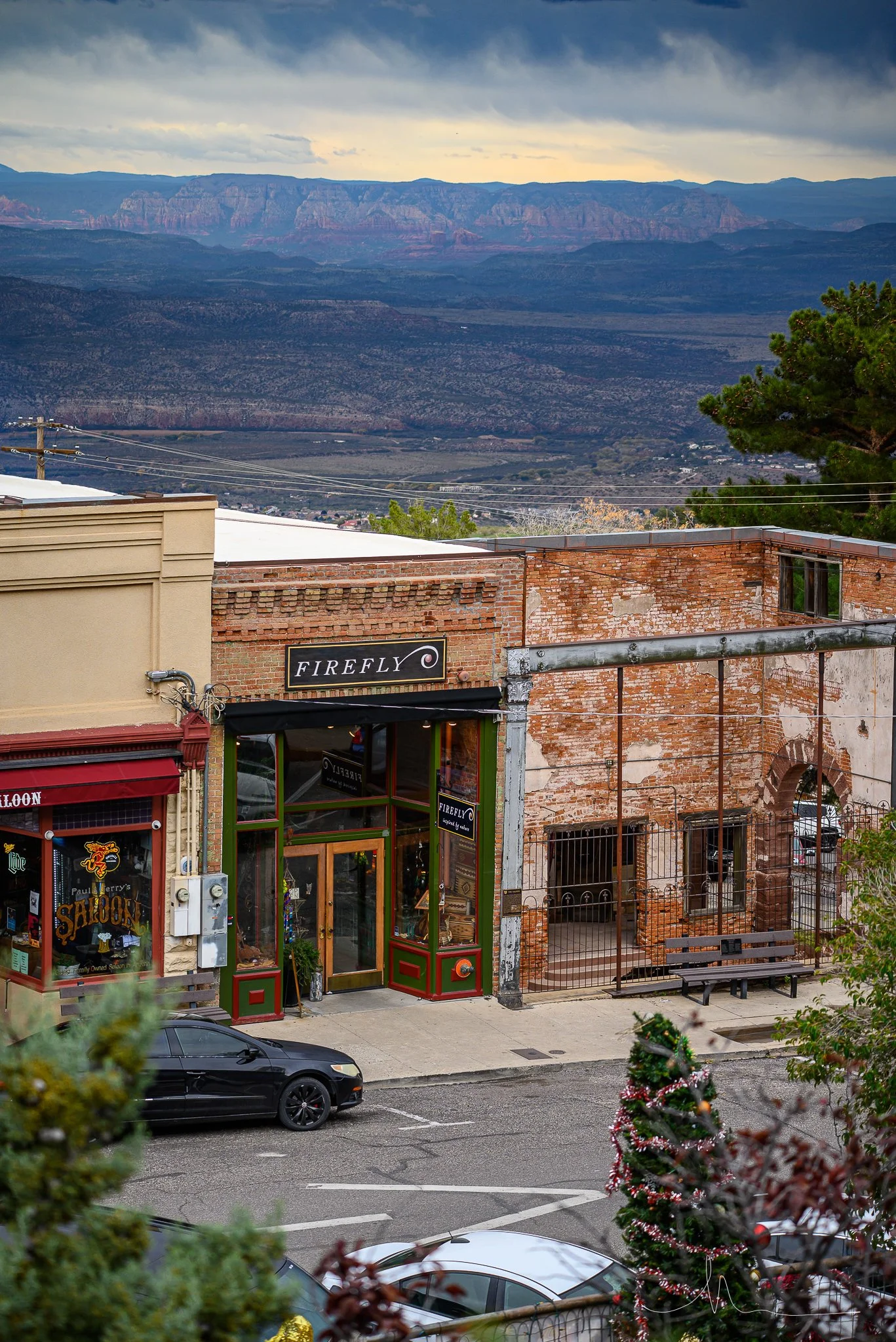 View of buildings with a sign for Firefly restaurant, parked cars in foreground, trees, and a mountain landscape in the background.