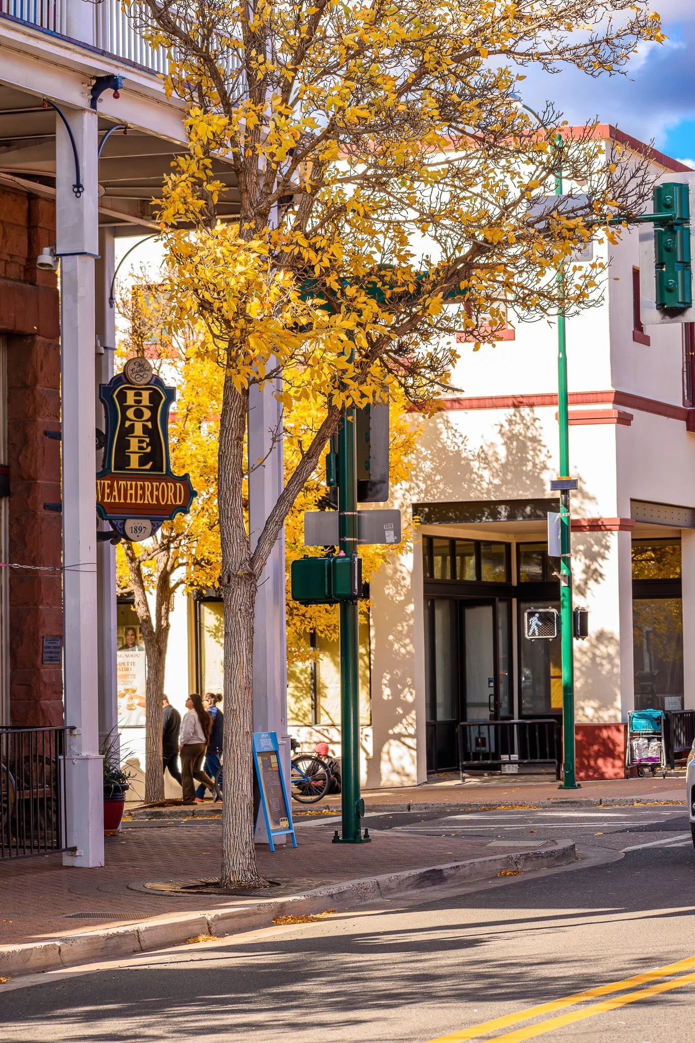 Street view with yellow autumn trees, building facades, and pedestrians walking along the sidewalk.