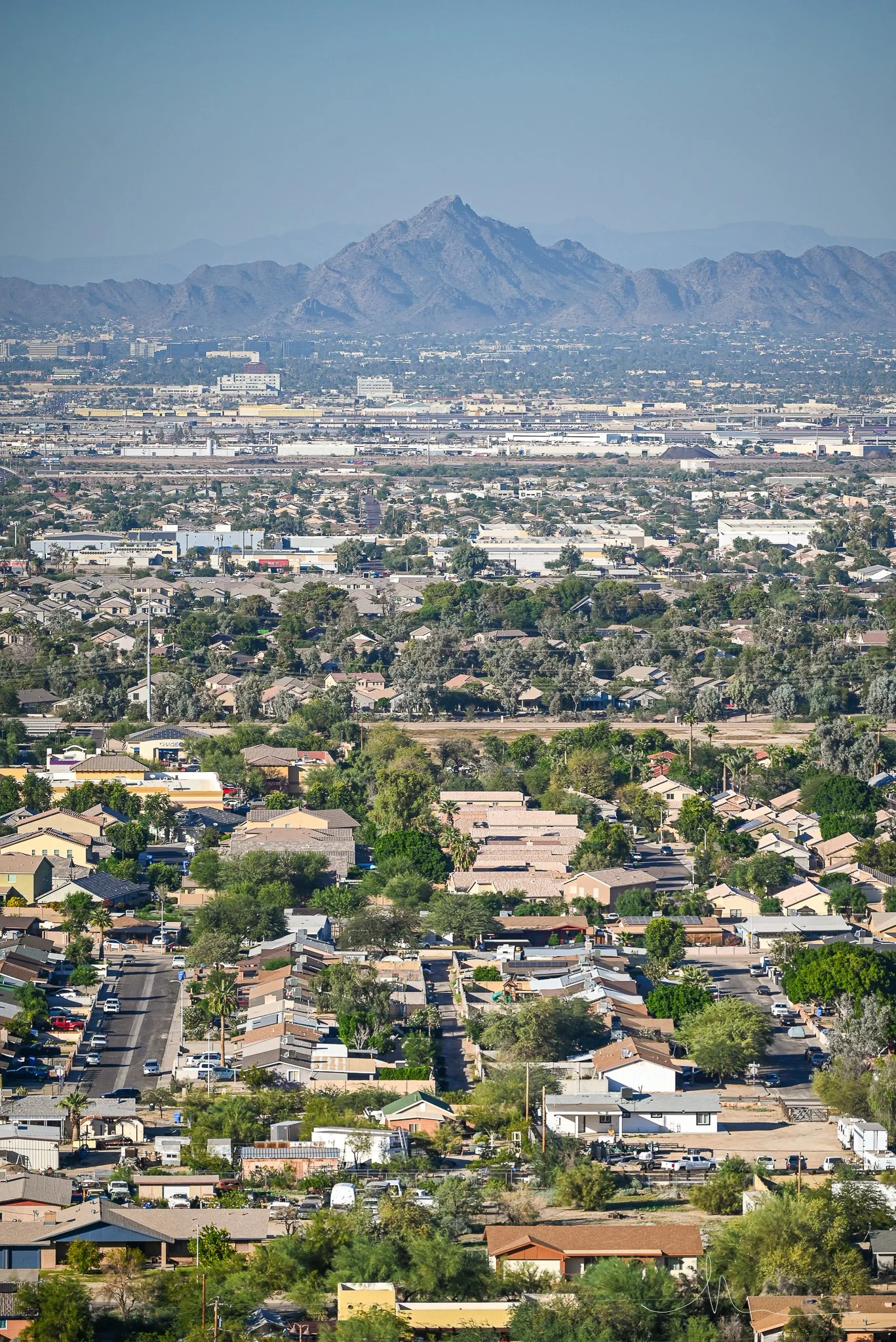 A cityscape with residential houses, commercial buildings, and distant mountains with a blue sky.
