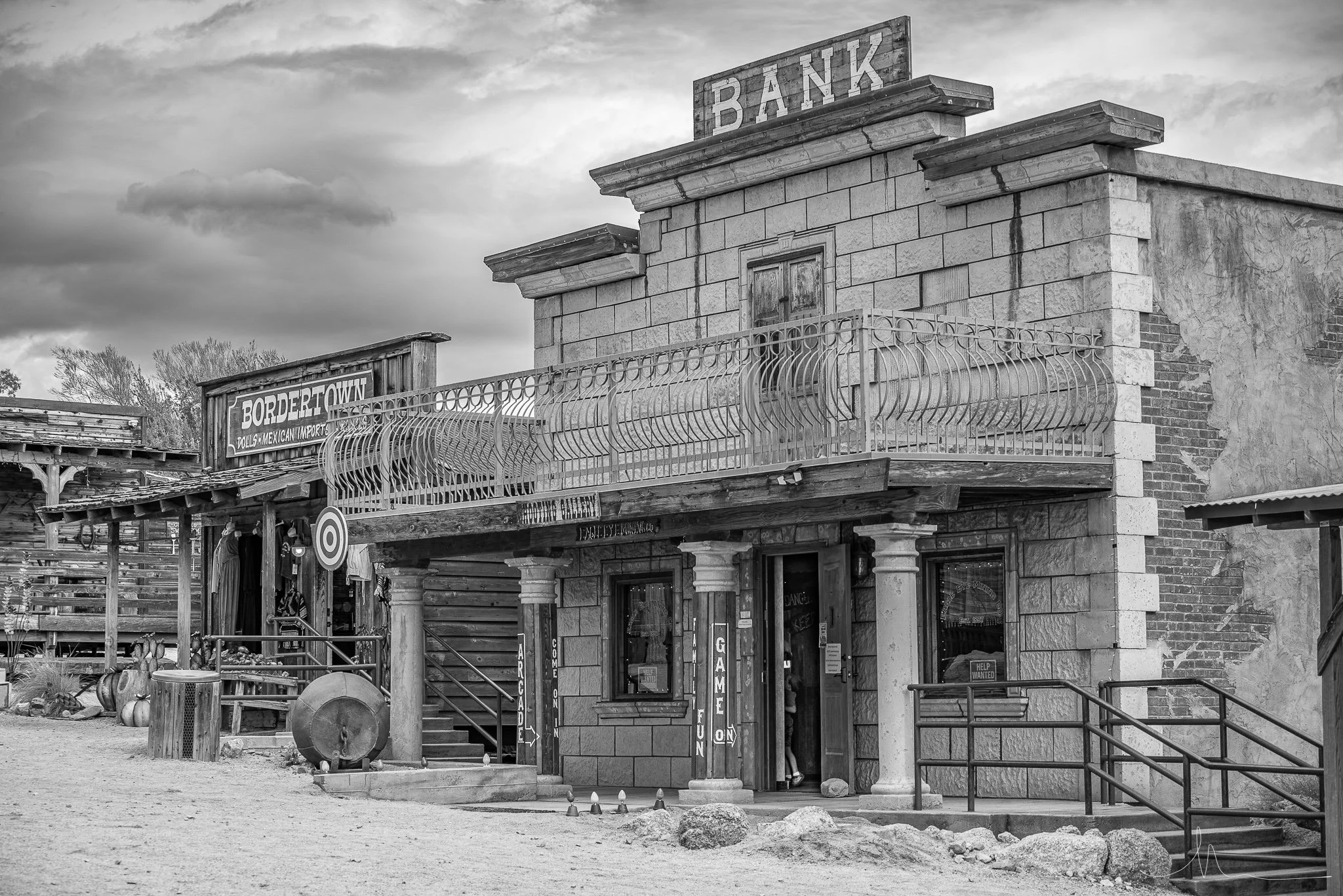 Old western-style building with a sign that reads 'BANK' on top, featuring stone walls, a balcony with a decorative railing, and a wooden door.