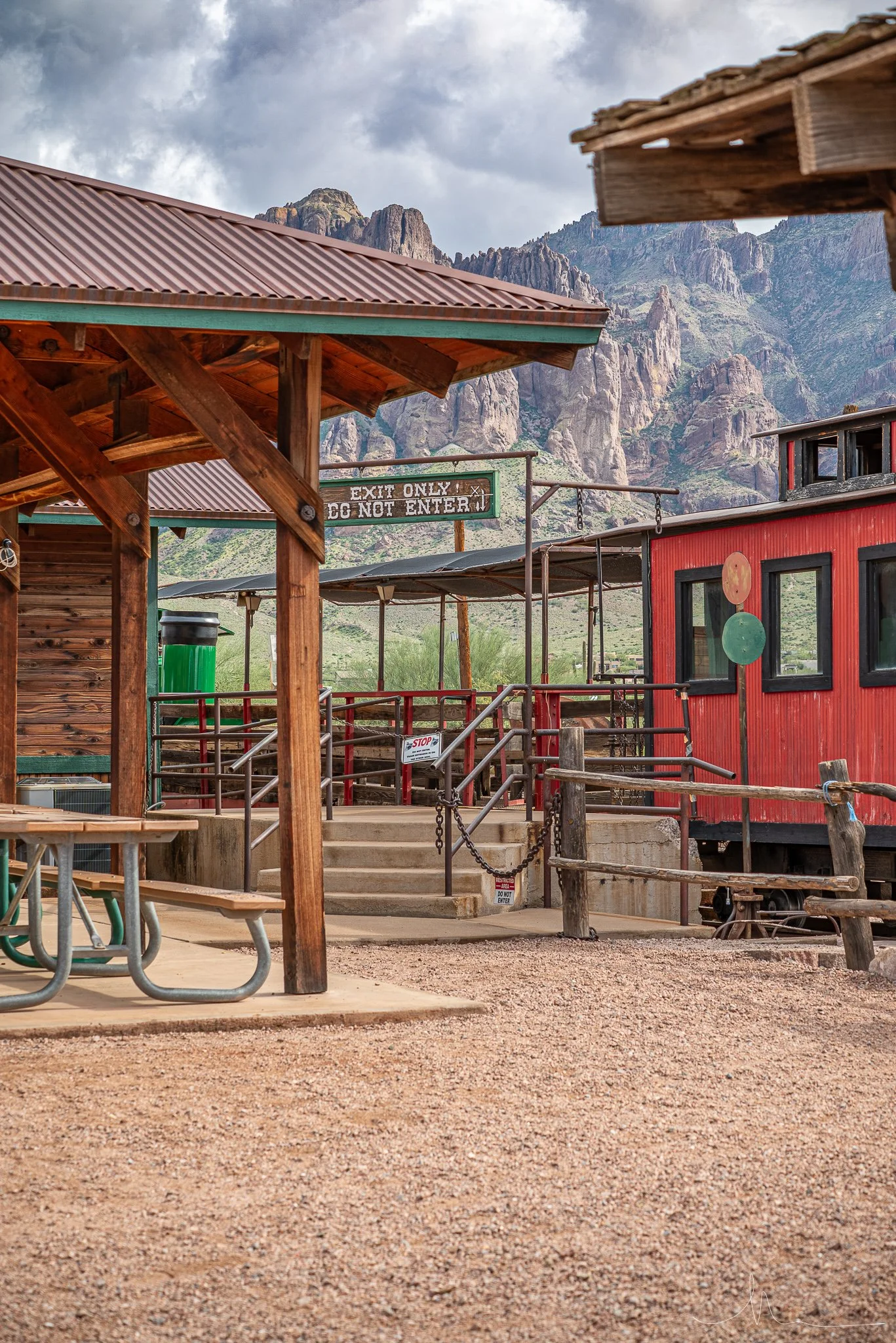 Outdoor scene with wooden and metal structures, a red building, stairs, and a mountain range in the background on a cloudy day.