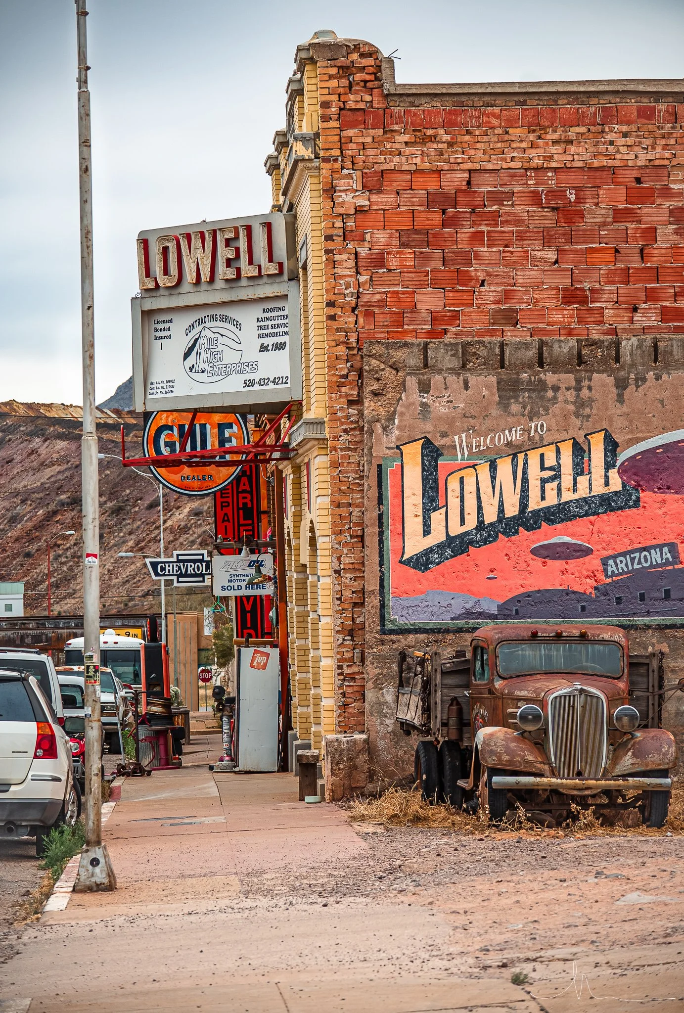 Street scene in Lowell, Arizona, with vintage signs, an old rusty truck, and brick buildings.