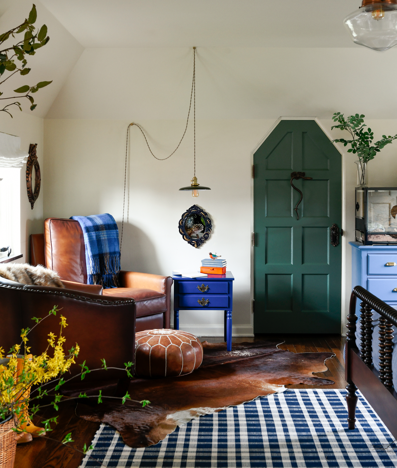 Cozy living room with leather armchair, blue side table, houseplants, cowhide rug, and a closed green door.